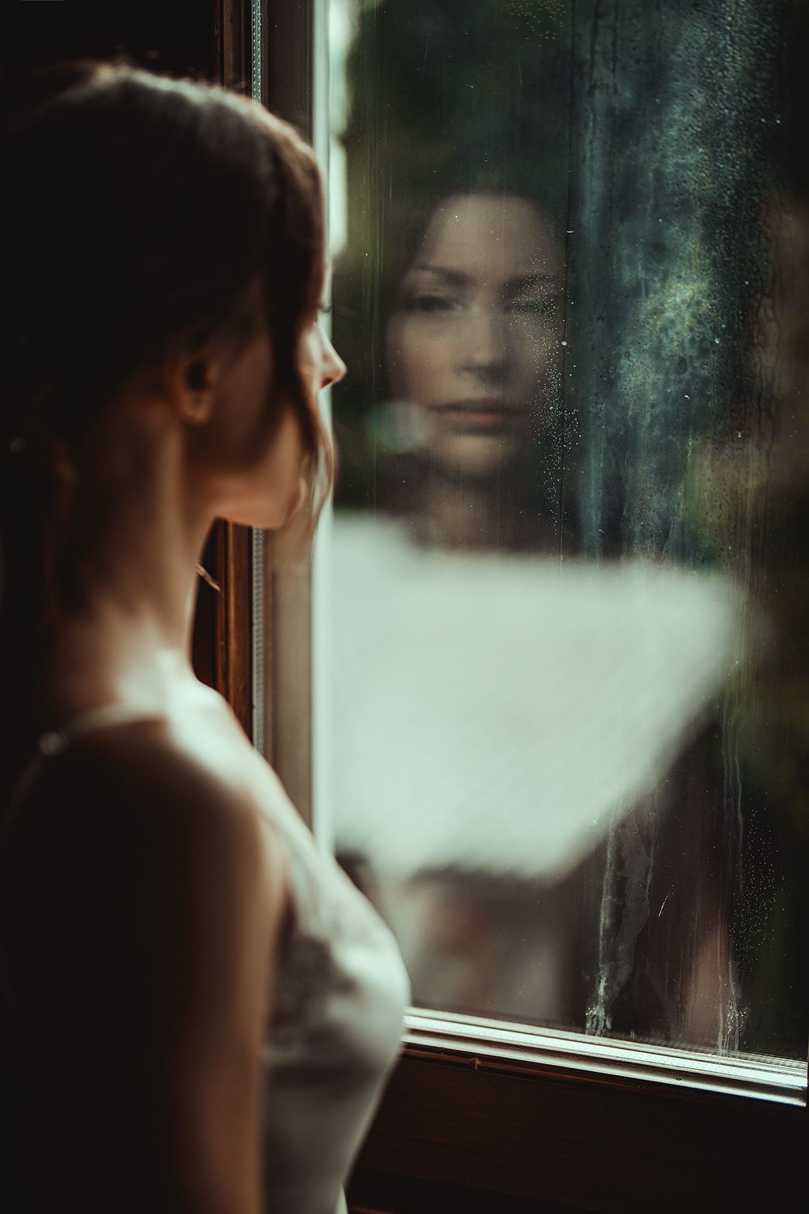 Moody reflection in window glass creates artistic double exposure effect with soft lighting and muted tones.