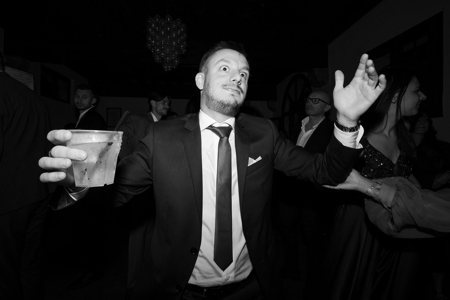 Wedding guests dancing and celebrating with dramatic lighting at an evening reception.