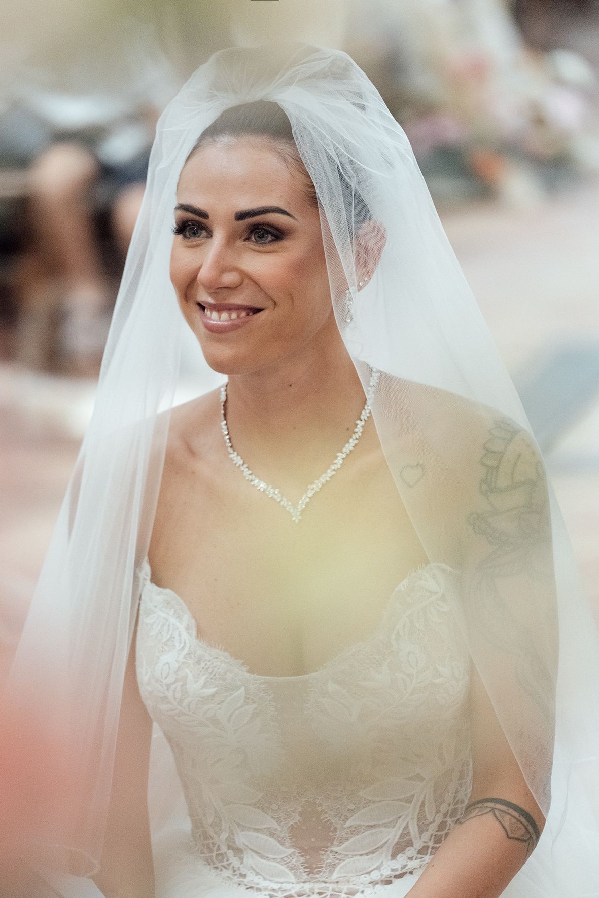 Close-up of bride wearing delicate lace dress and veil with pearl necklace.