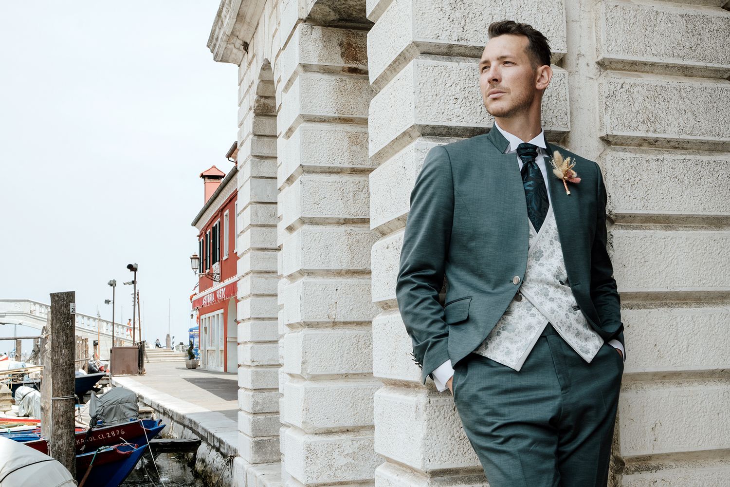 Groom poses elegantly against classical stone architecture.