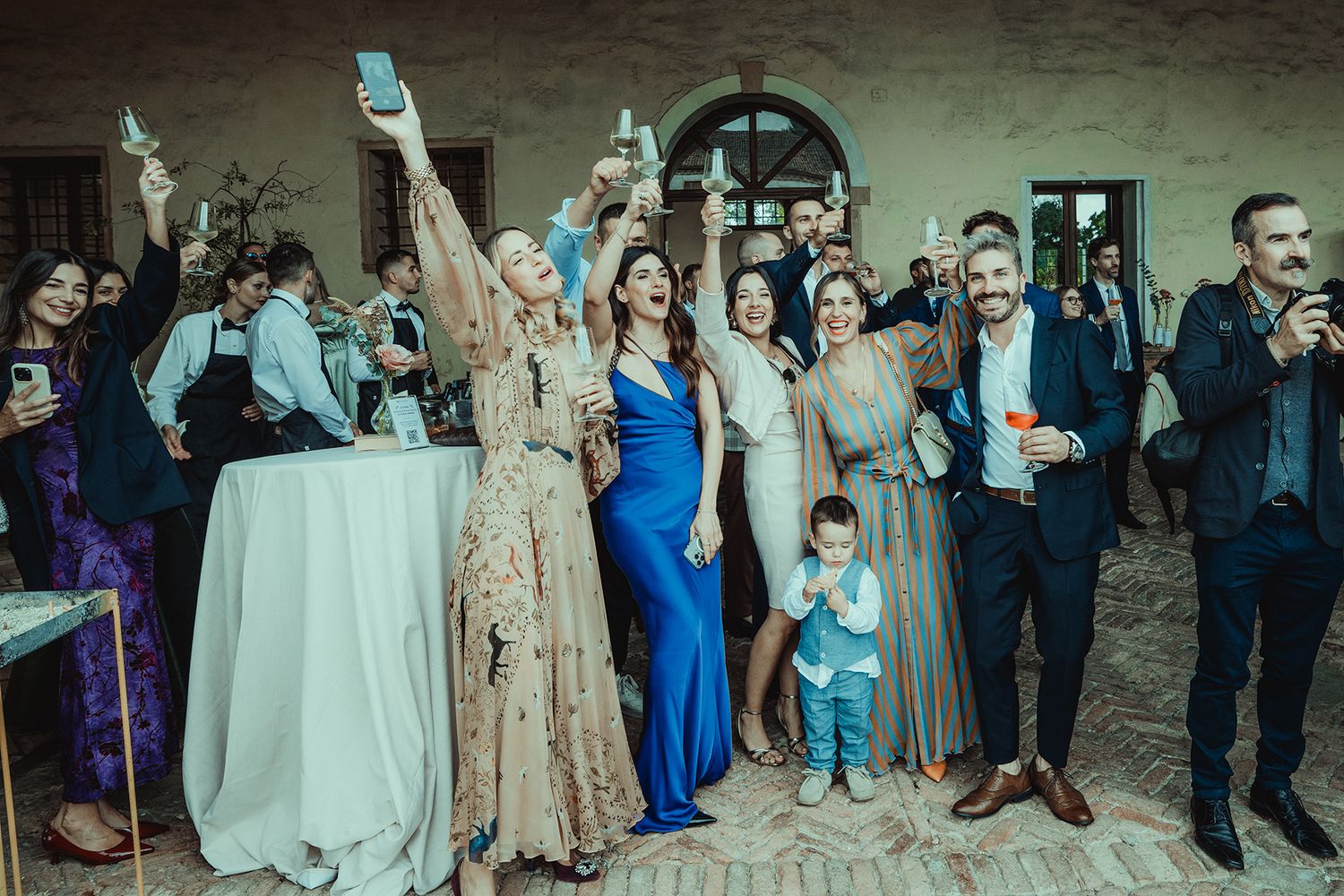 Wedding party and guests gather for group photo outside historic building.