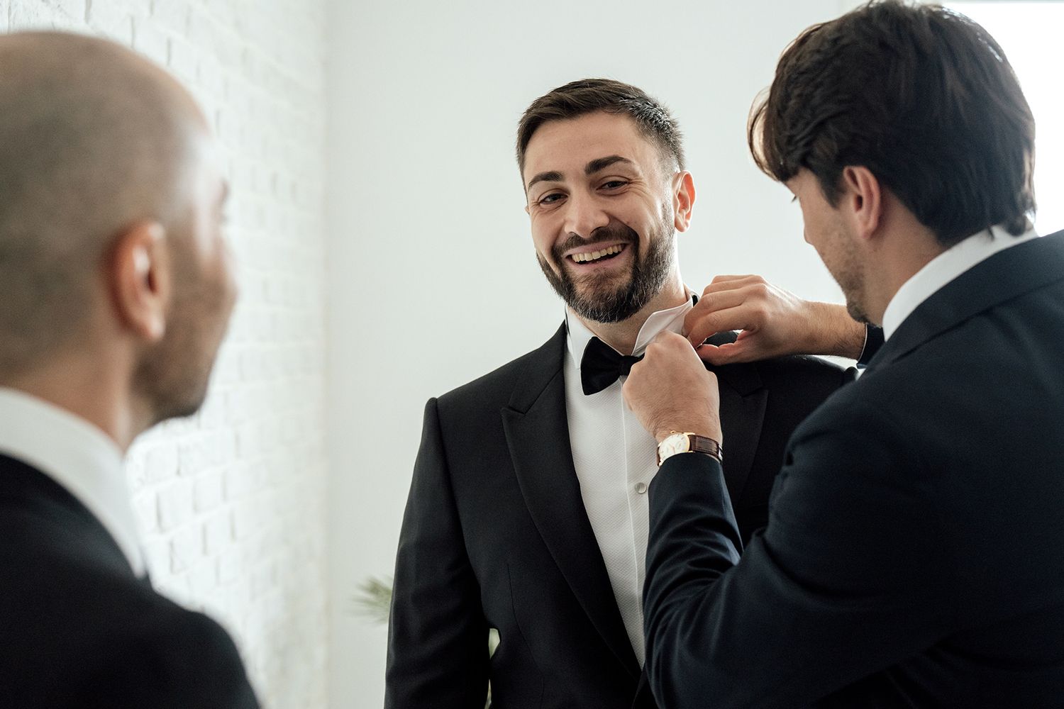 Men in formal suits sharing joyful moments against white background in natural lighting.