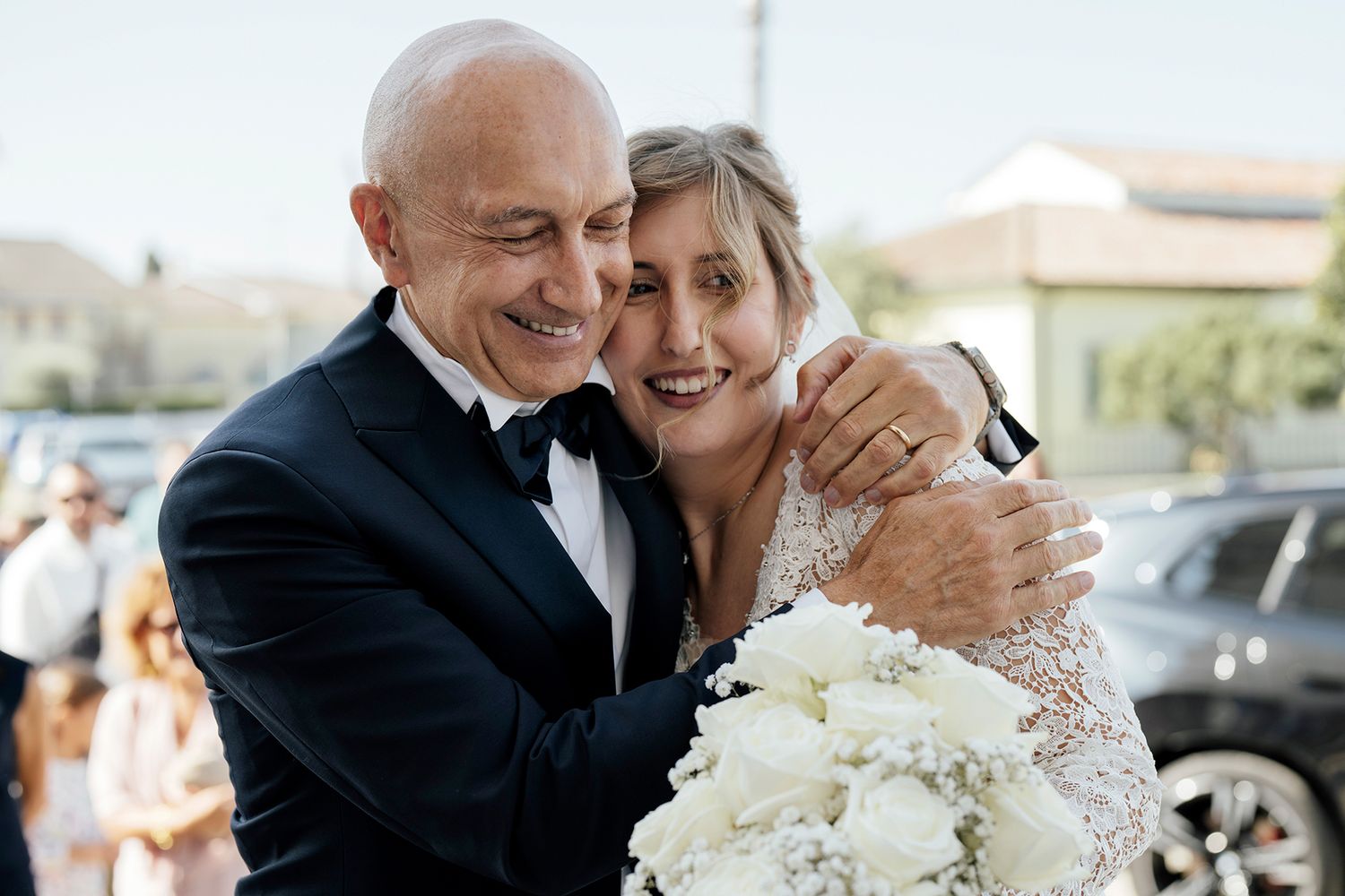 Joyful wedding couple embracing while holding white floral bouquet.