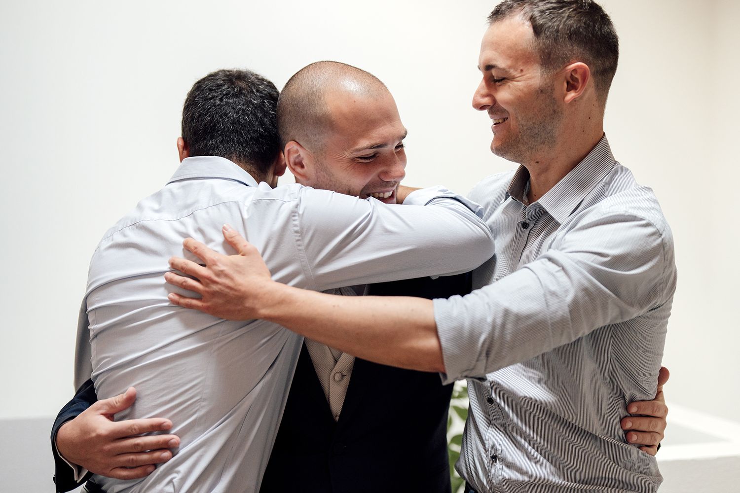 Three men in formal wear share warm group hug during celebration.