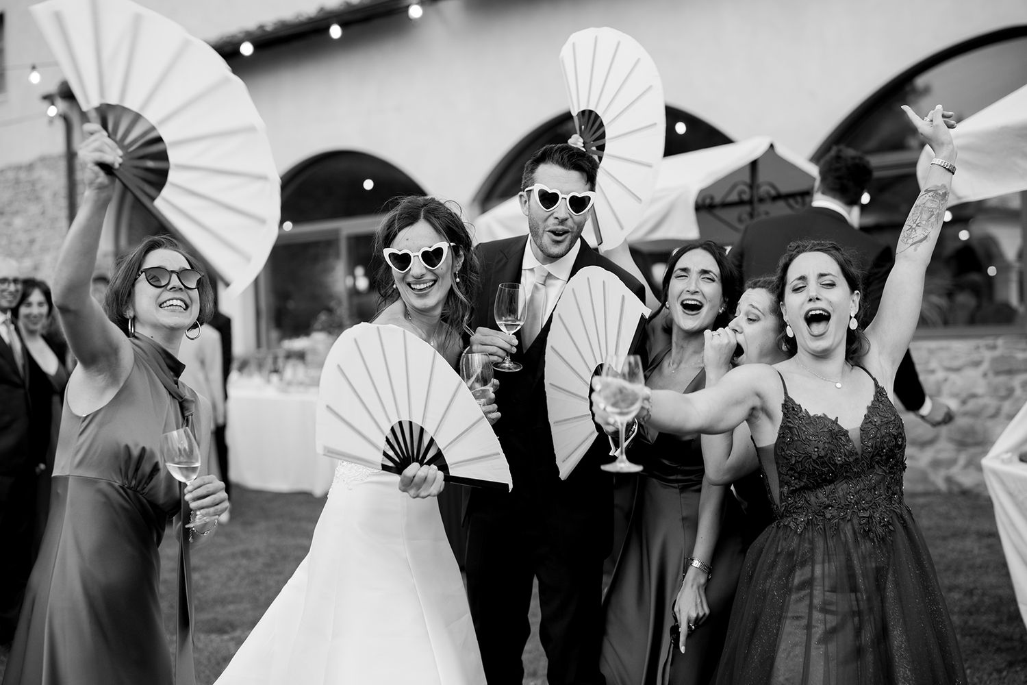 Wedding party holding decorative white paper fans while posing together outdoors.