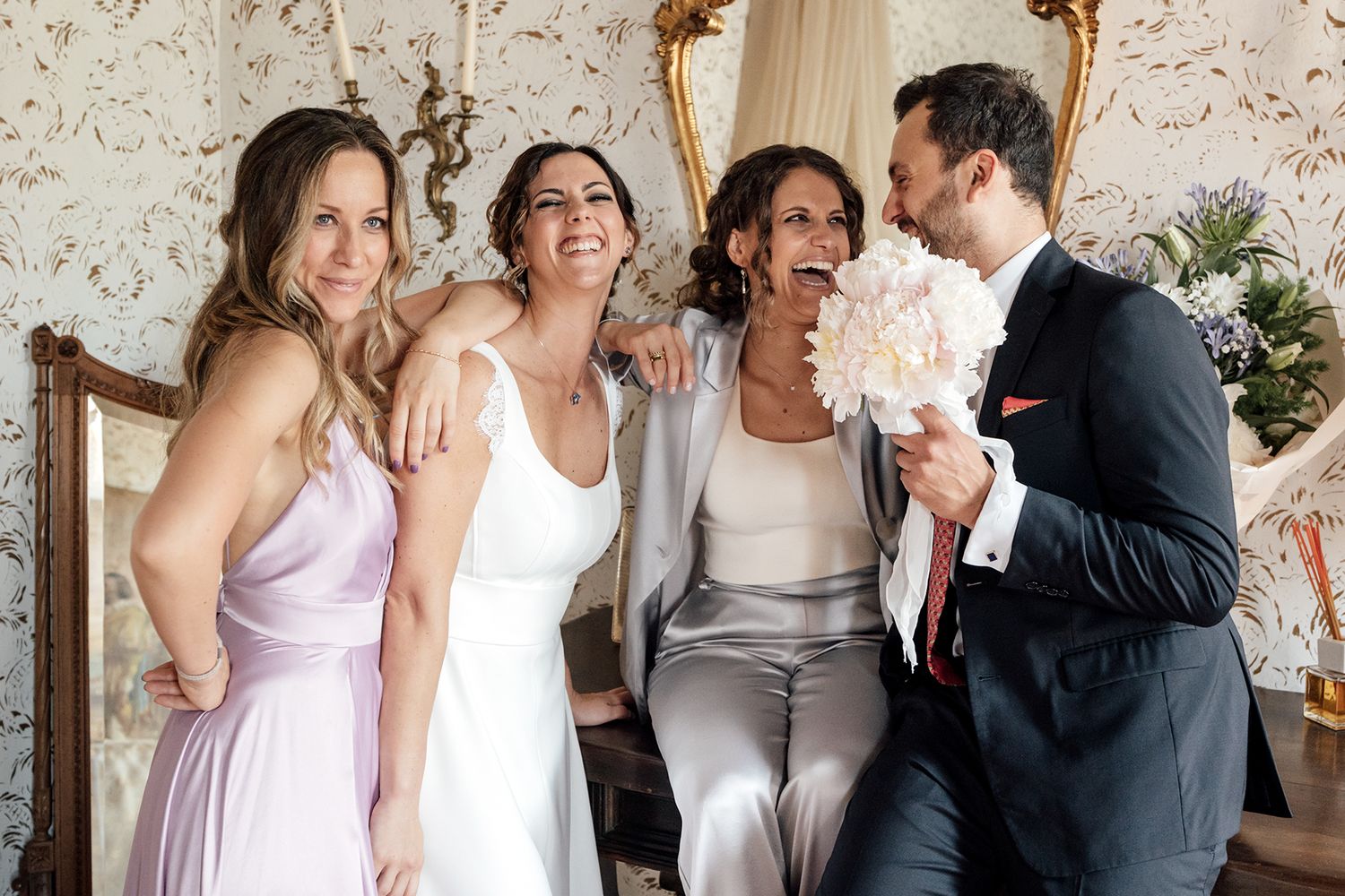 Wedding party gathering in a vintage-styled room with floral wallpaper and elegant decor.