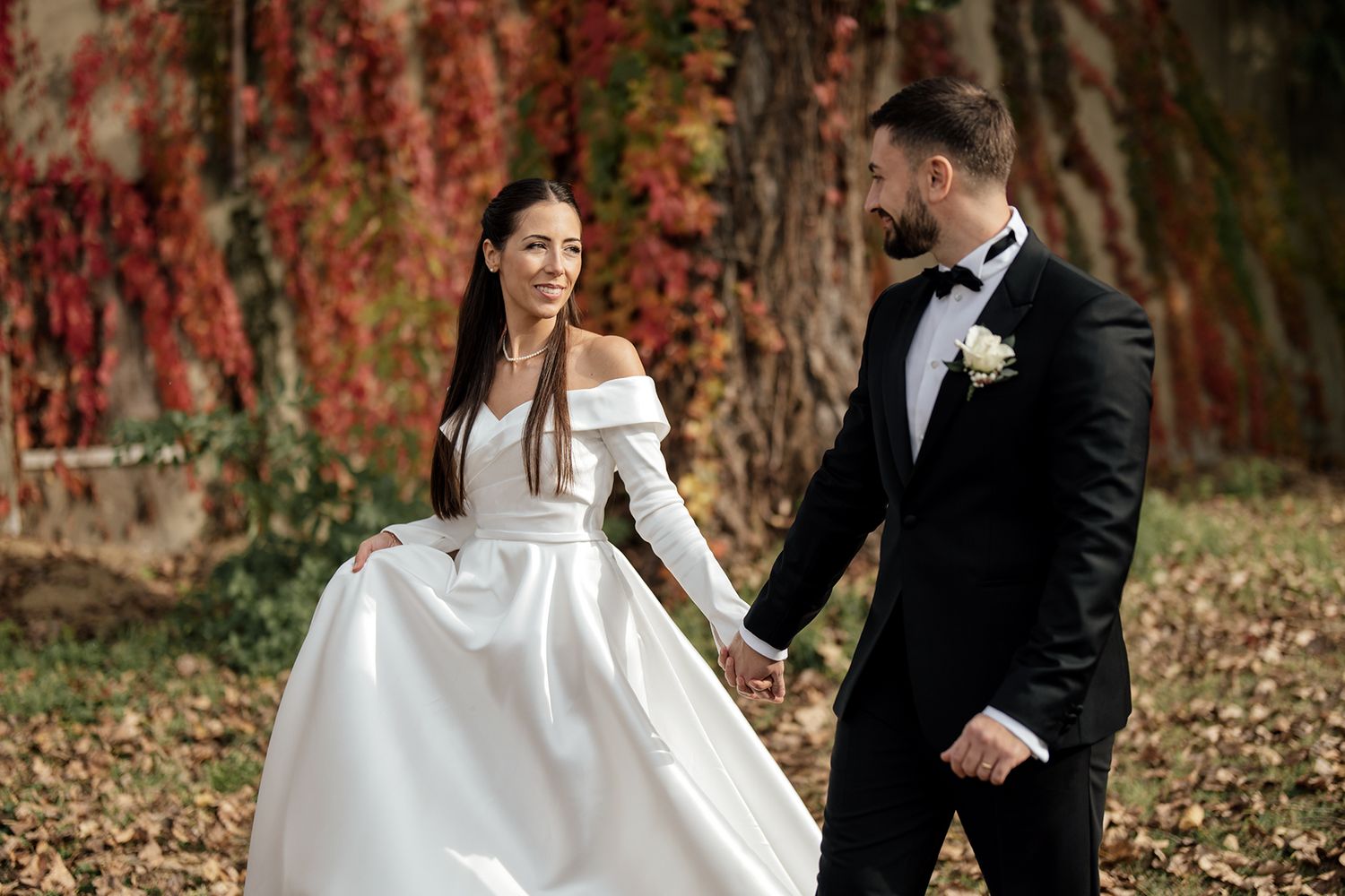 Wedding couple walking through autumn foliage with red ivy covered walls.