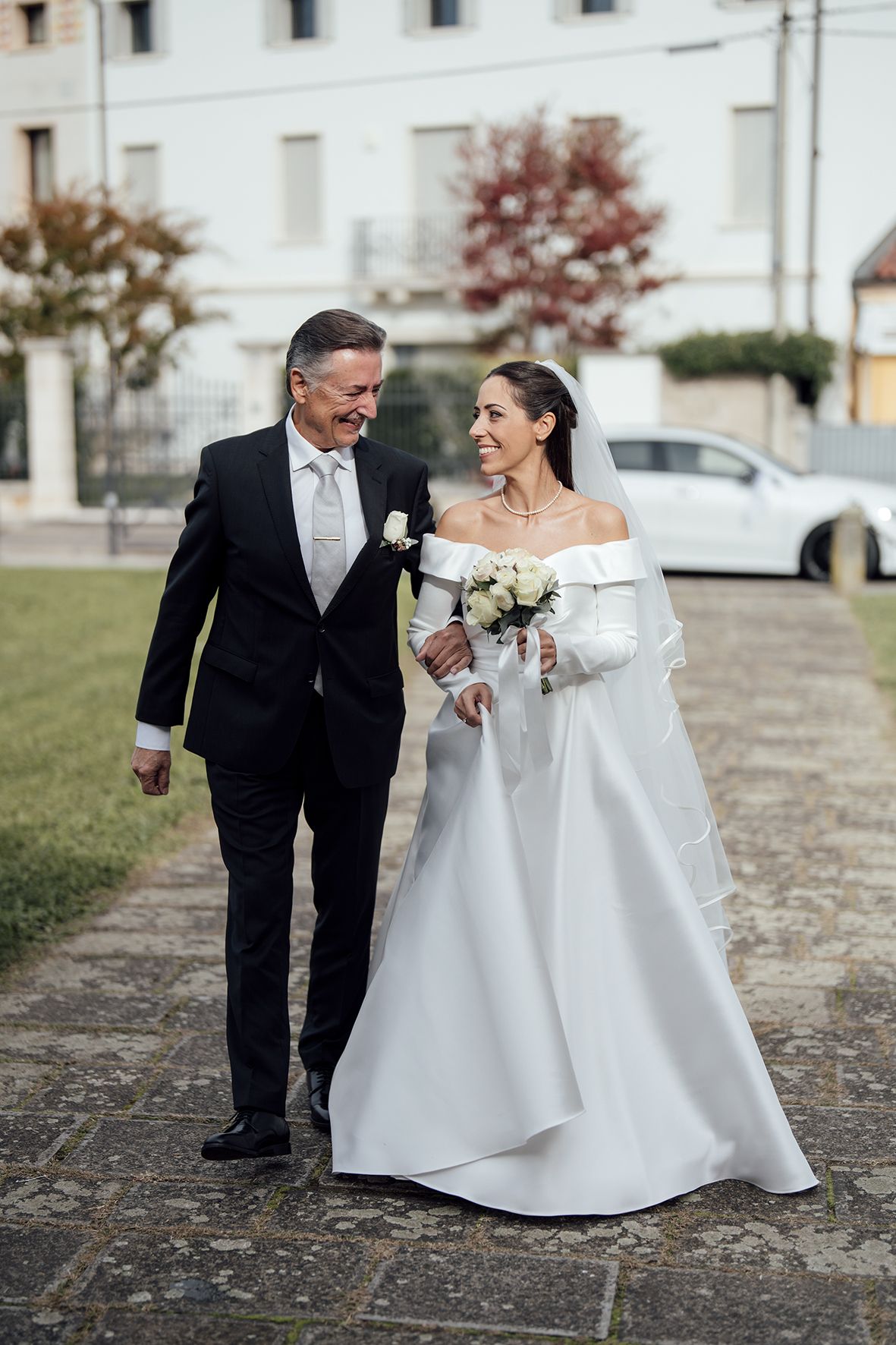 Wedding couple walking together outdoors, bride in dramatic white gown and groom in classic black tuxedo.