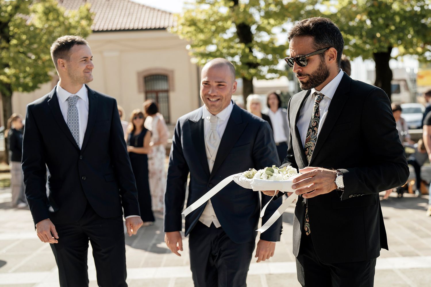 Groomsmen in dark suits sharing a lighthearted moment outdoors.