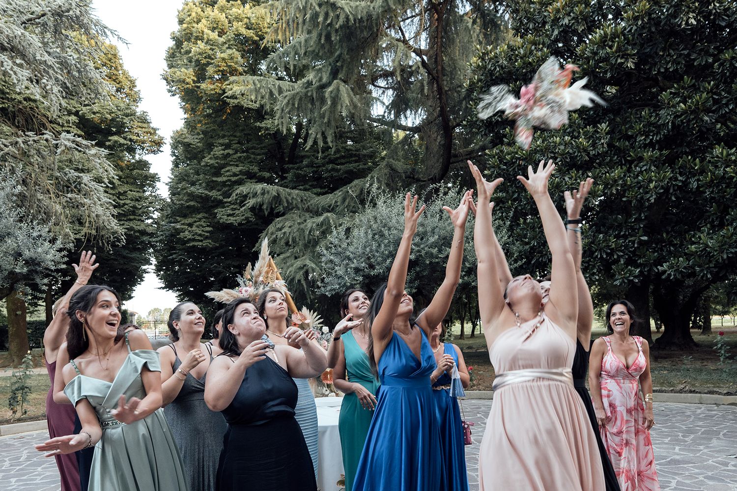 Wedding party guests dancing and celebrating outdoors with raised arms in colorful dresses.