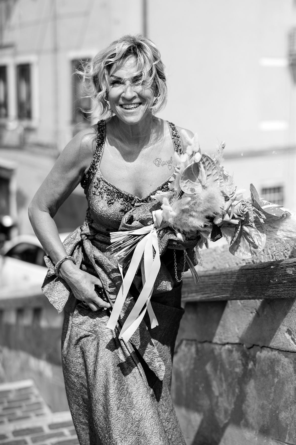 Woman in sparkly dress leaning against rustic wooden railing with decorative ribbons.