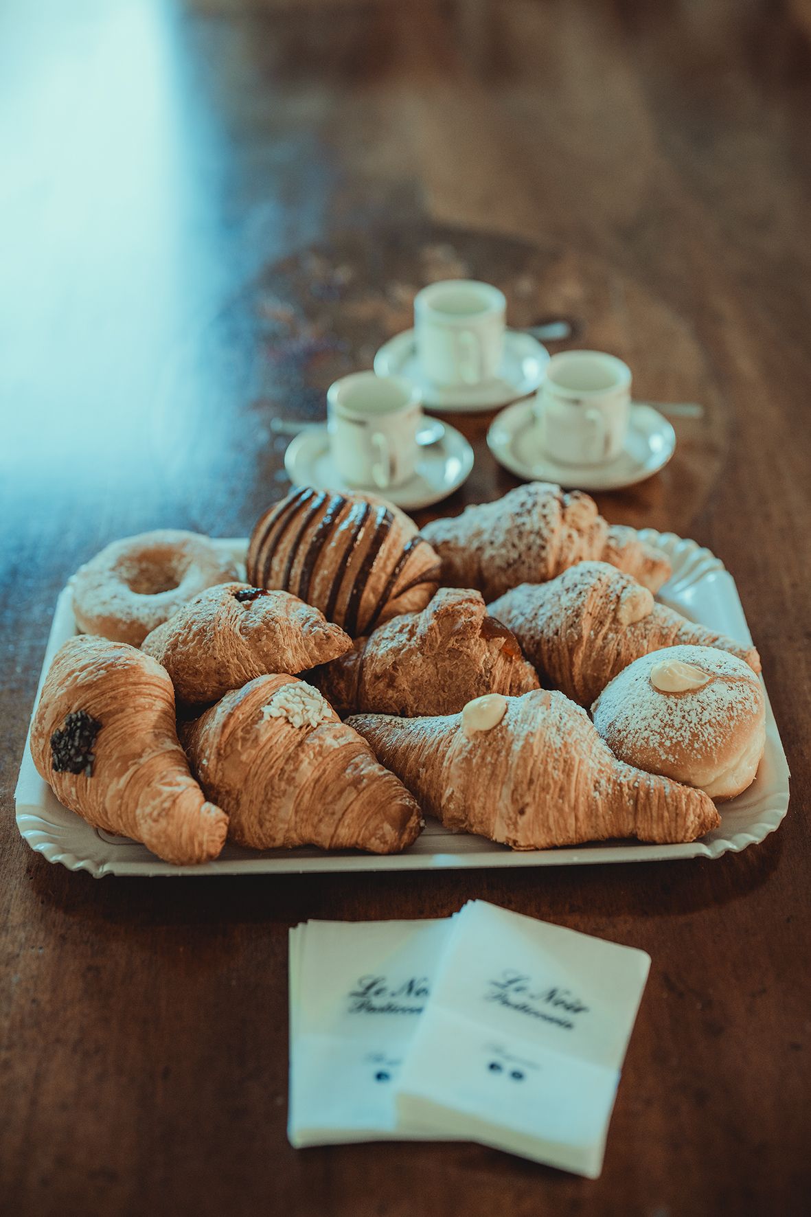 Fresh croissants and pastries arranged on wooden table with coffee cups.
