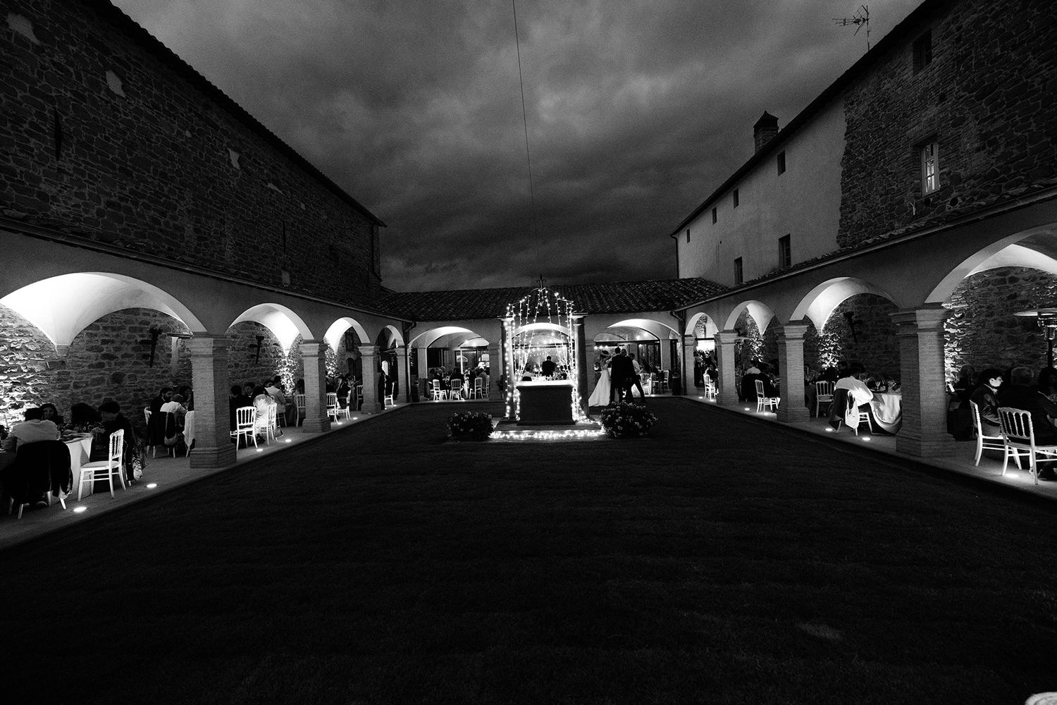 Panoramic nighttime view of an illuminated stone villa with arched walkways.