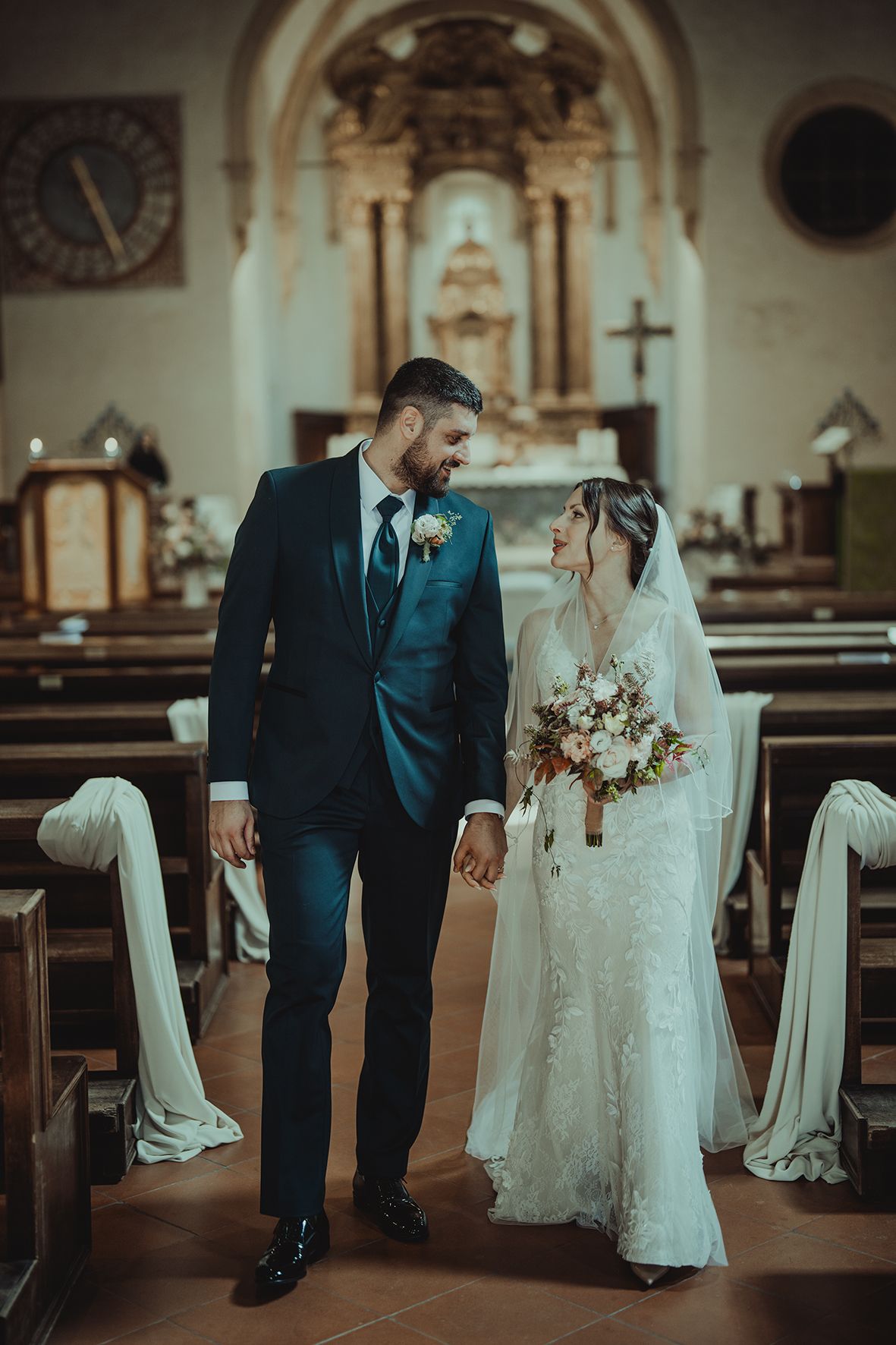 A couple shares an intimate moment in a historic church with ornate altar and decorated pews.