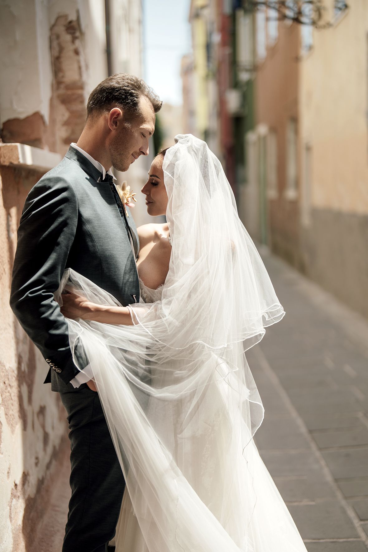 Wedding couple interacts with flowing veil in charming Italian street setting.