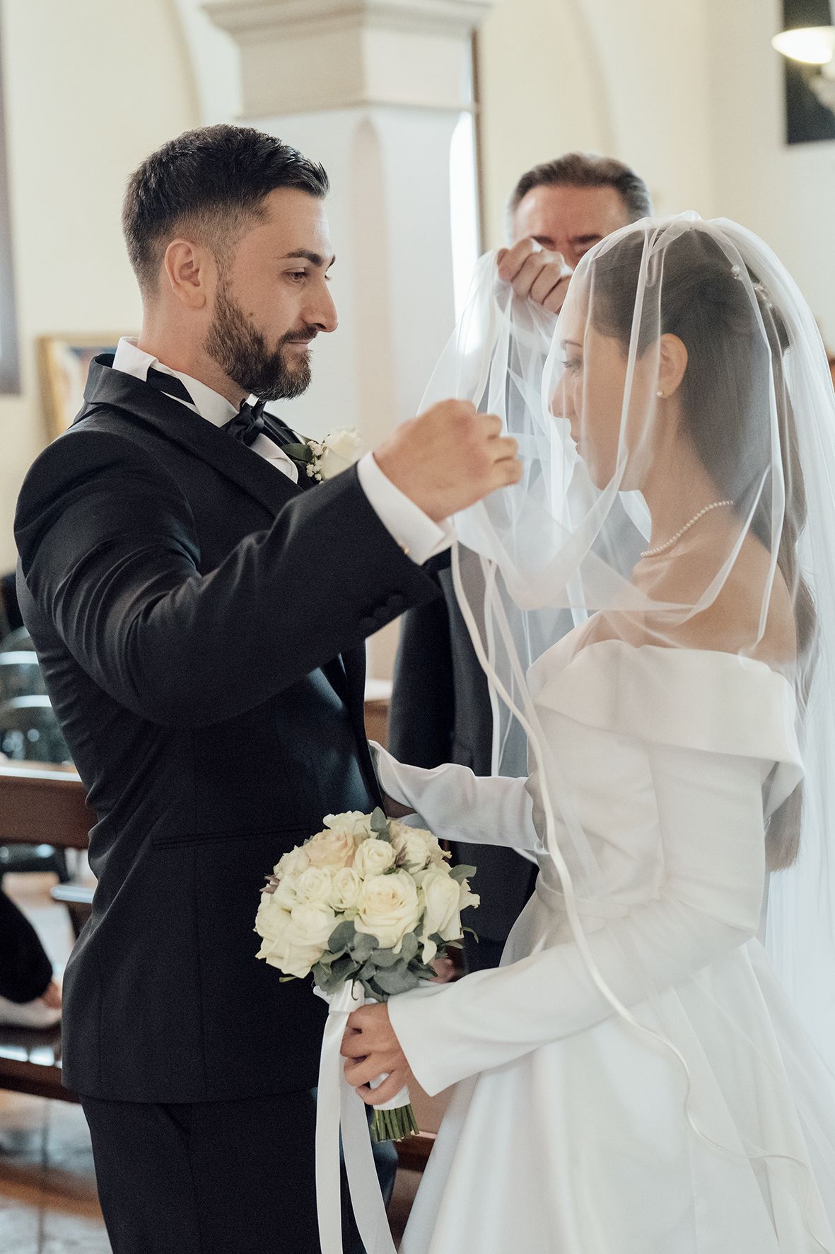 Tender moments between newlyweds in white dress and black tuxedo during church ceremony.