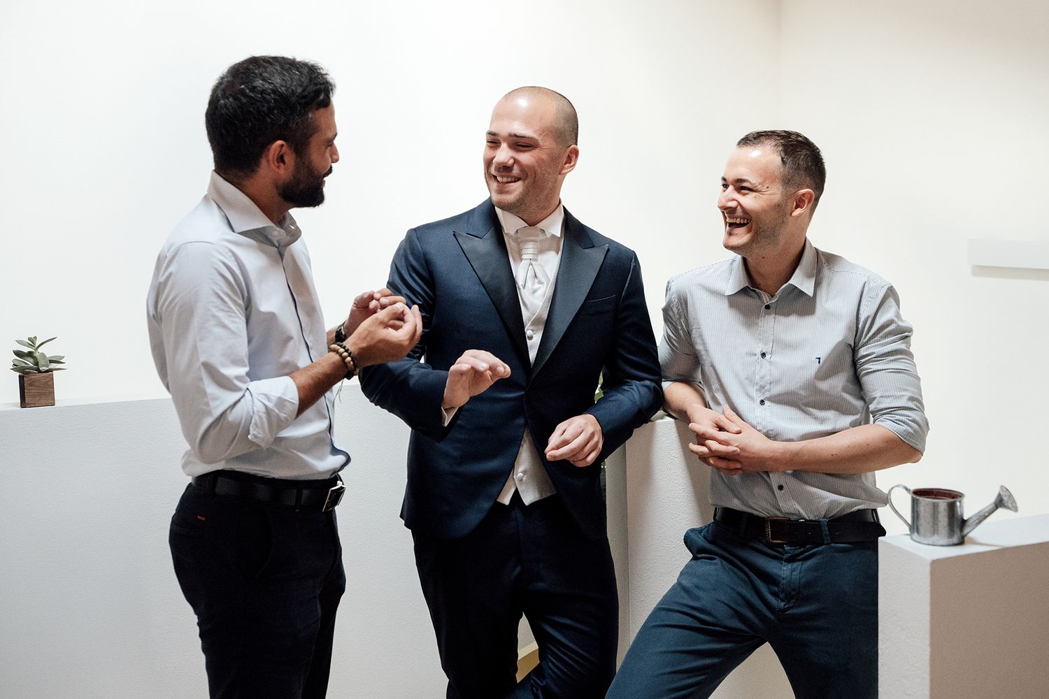 Three friends in formal attire share animated conversation and laughter in bright room.