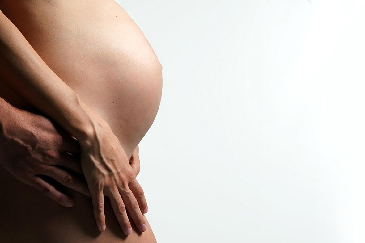 Close-up side view of pregnant belly with hands gently cradling the bump.