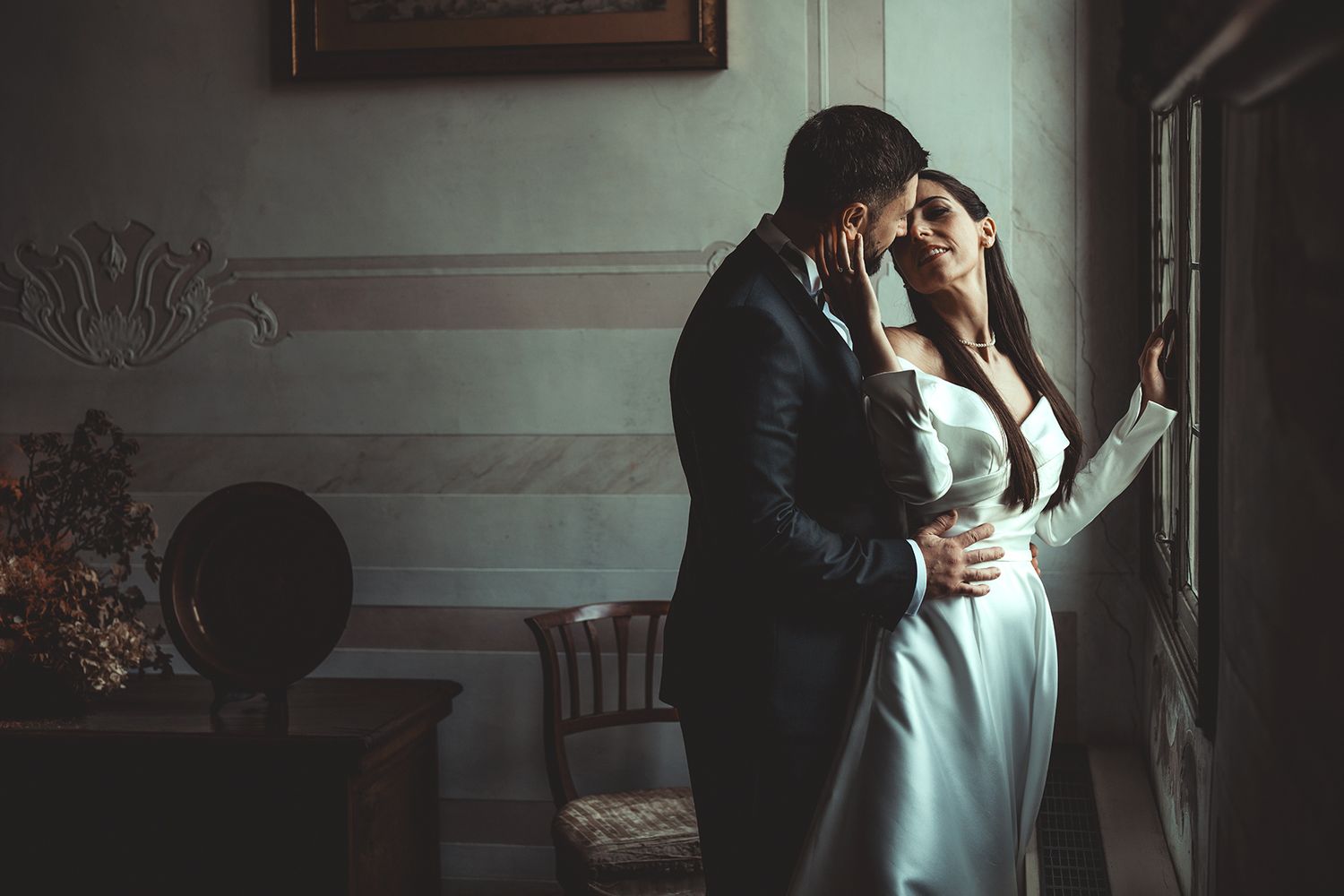 Atmospheric wedding photos capturing tender moments between a couple in a dimly lit room.
