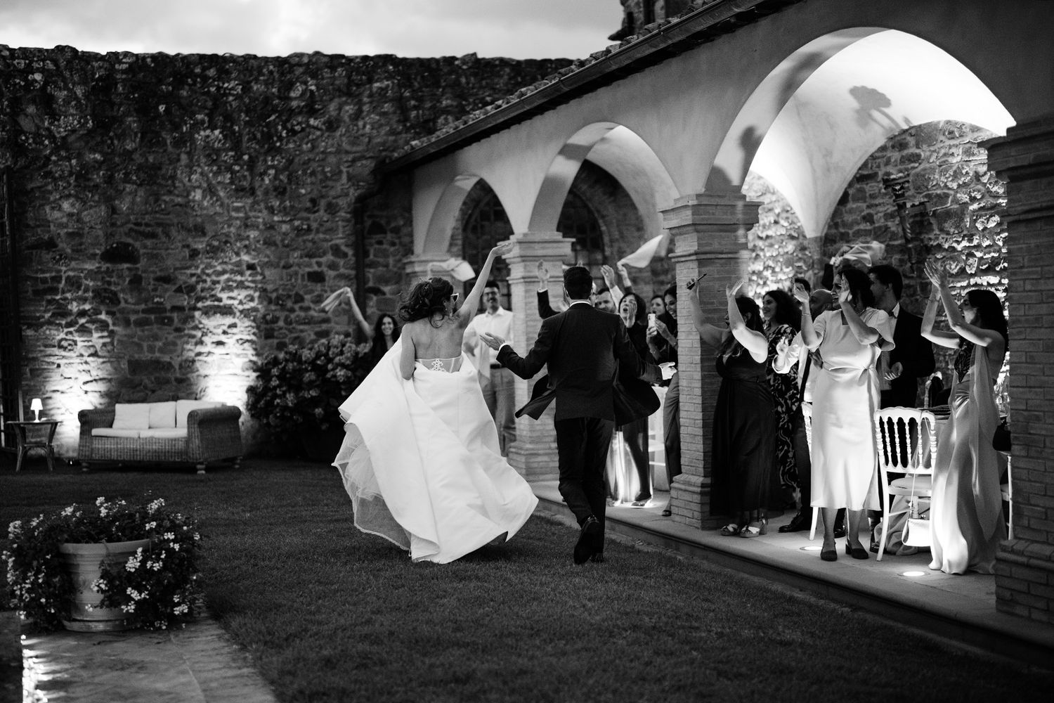 Black and white wedding reception scene under arched stone architecture with dramatic lighting.
