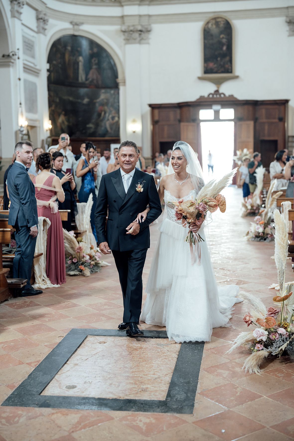 Wedding ceremony in progress inside an ornate white church with floral decorations.