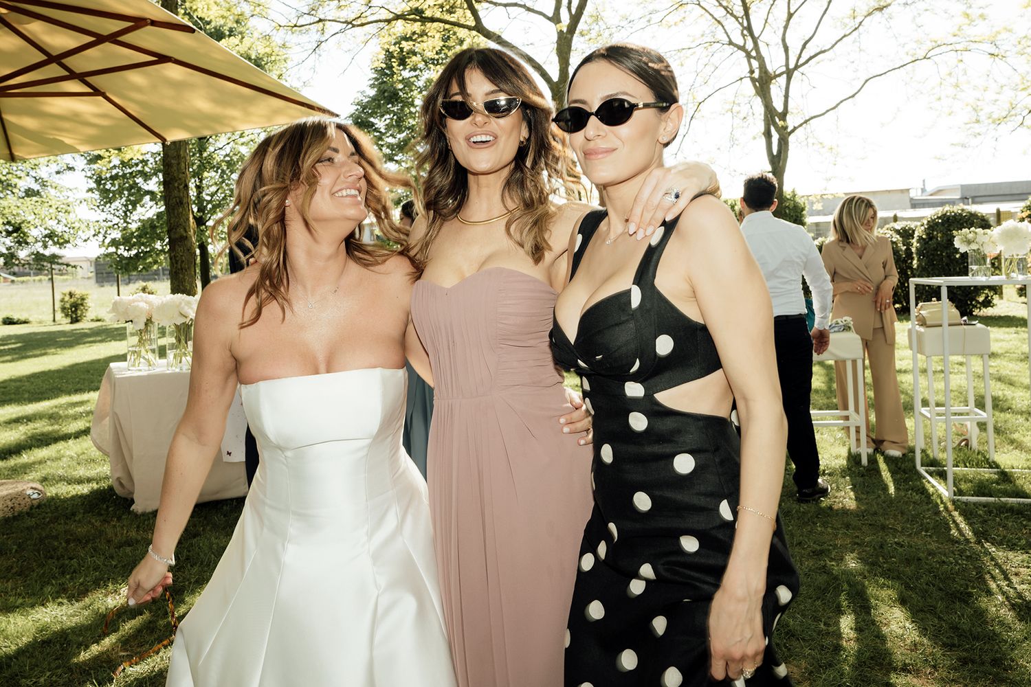 Wedding party in coordinated dresses posing under trees at outdoor venue.