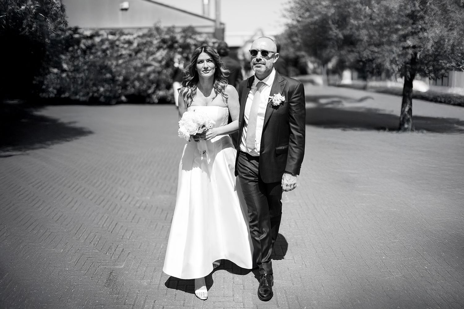 A black and white photo of a couple in wedding attire walking together outdoors.