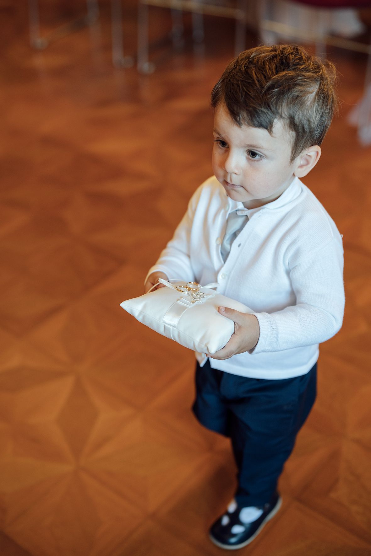Young ring bearer in formal attire on wooden floor at wedding event.