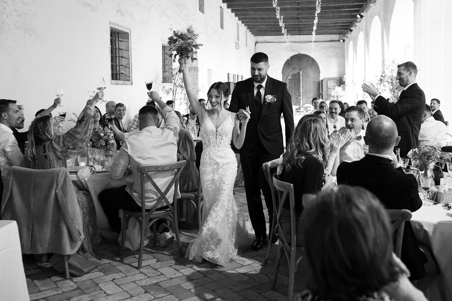 Black and white reception photo of couple walking through venue while guests celebrate.