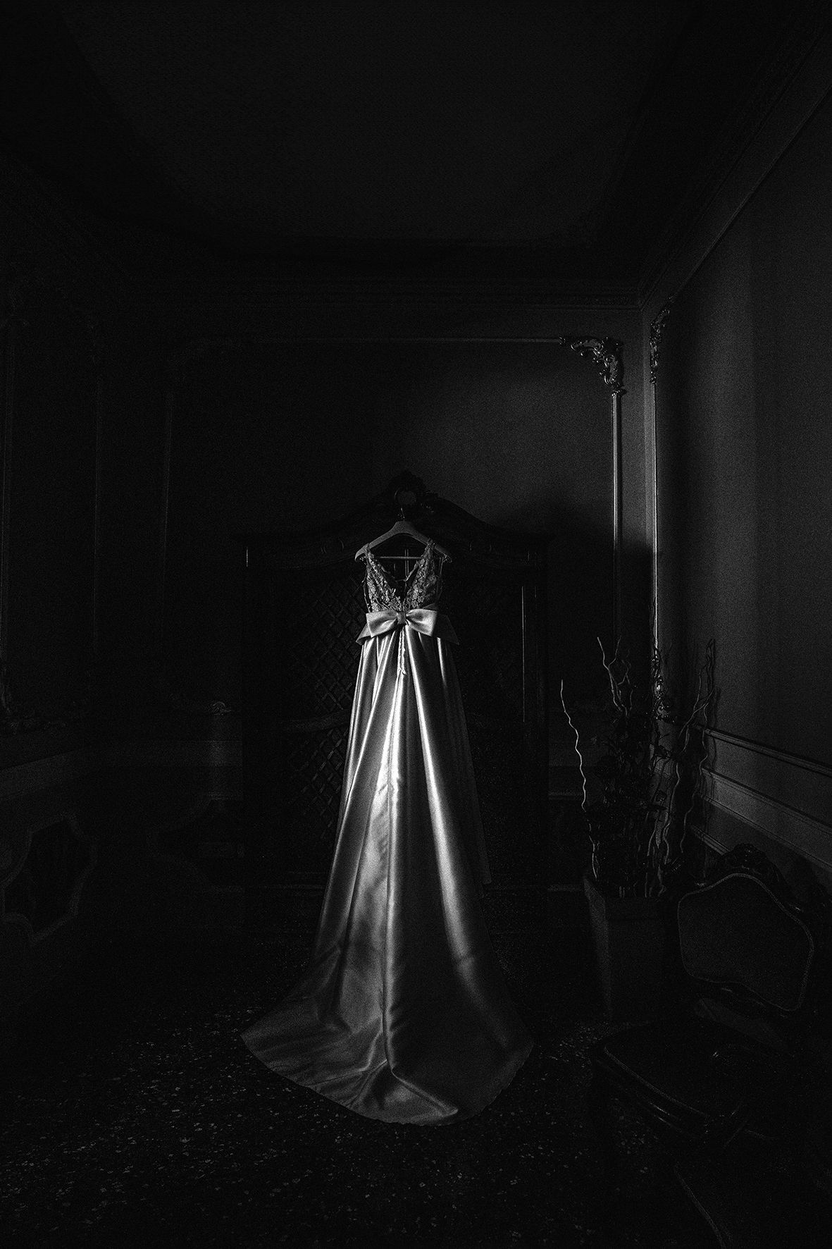 A dramatic black and white photograph of an elegant wedding dress standing alone in a dark, moody room.