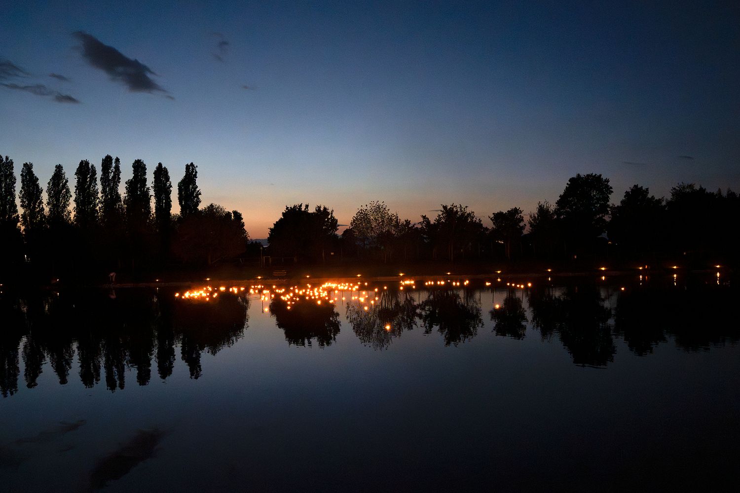 Silhouette of city skyline at dusk reflecting on calm water.