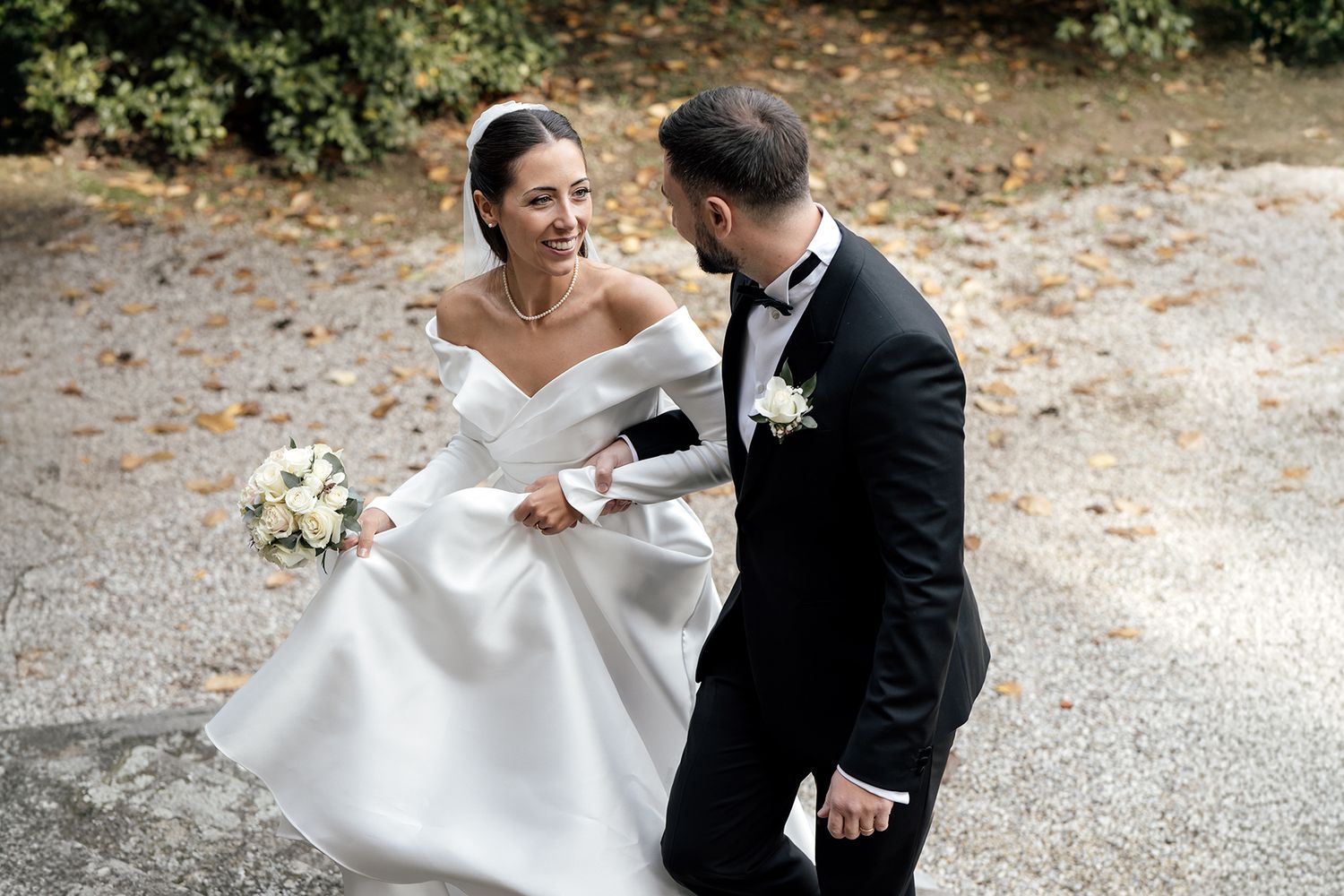 A couple shares a romantic moment outdoors in wedding attire with the bride in an elegant white dress.