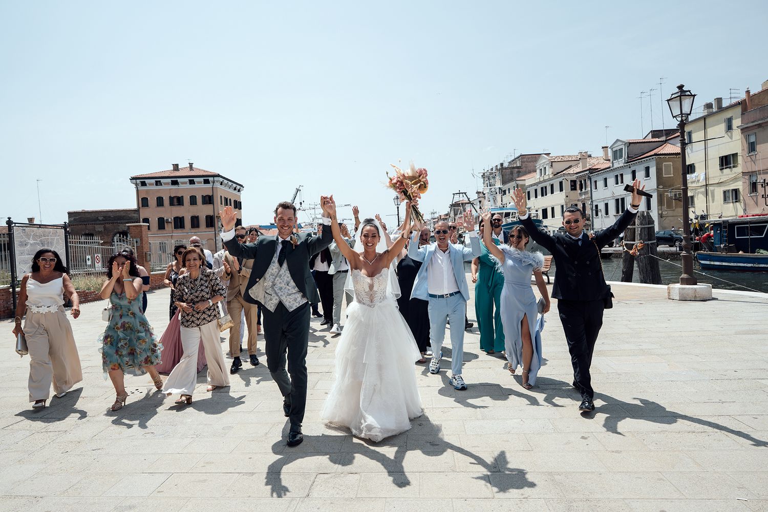 Wedding party performs synchronized dance moves outdoors with buildings in background.