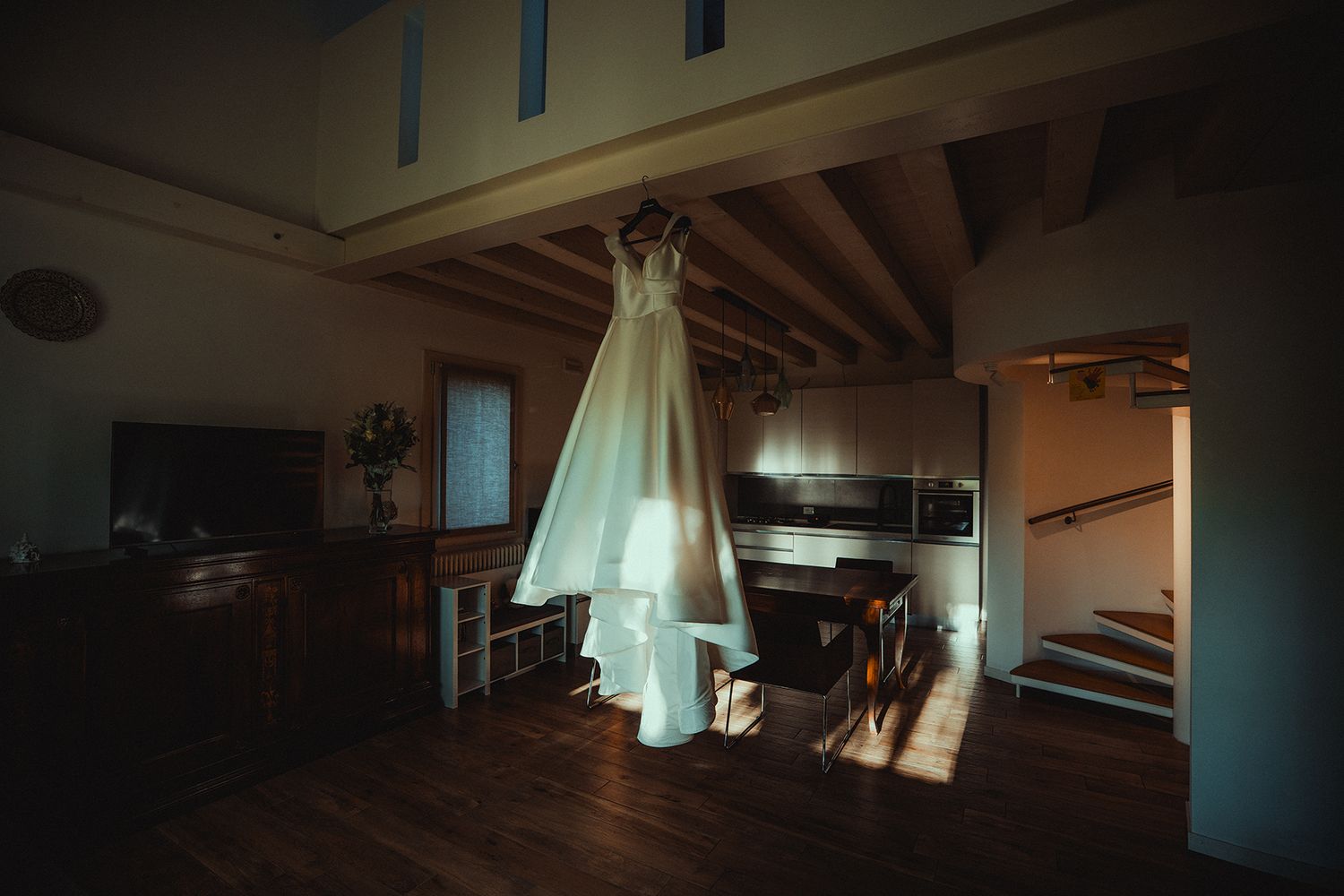 Wedding dress displayed in dark room with ambient lighting creating shadows.
