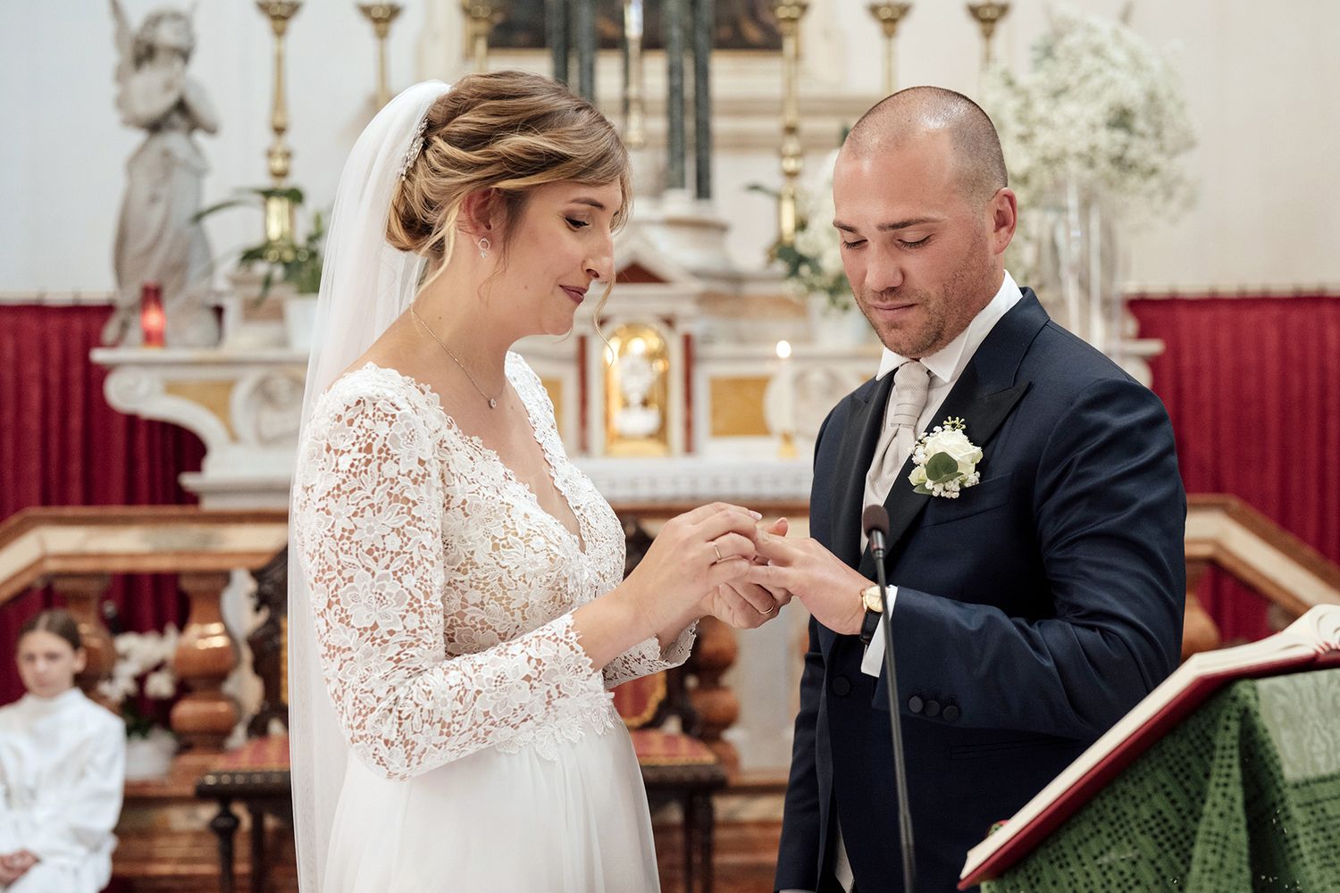 Wedding couple exchanges rings during their ceremony in an ornate church setting.