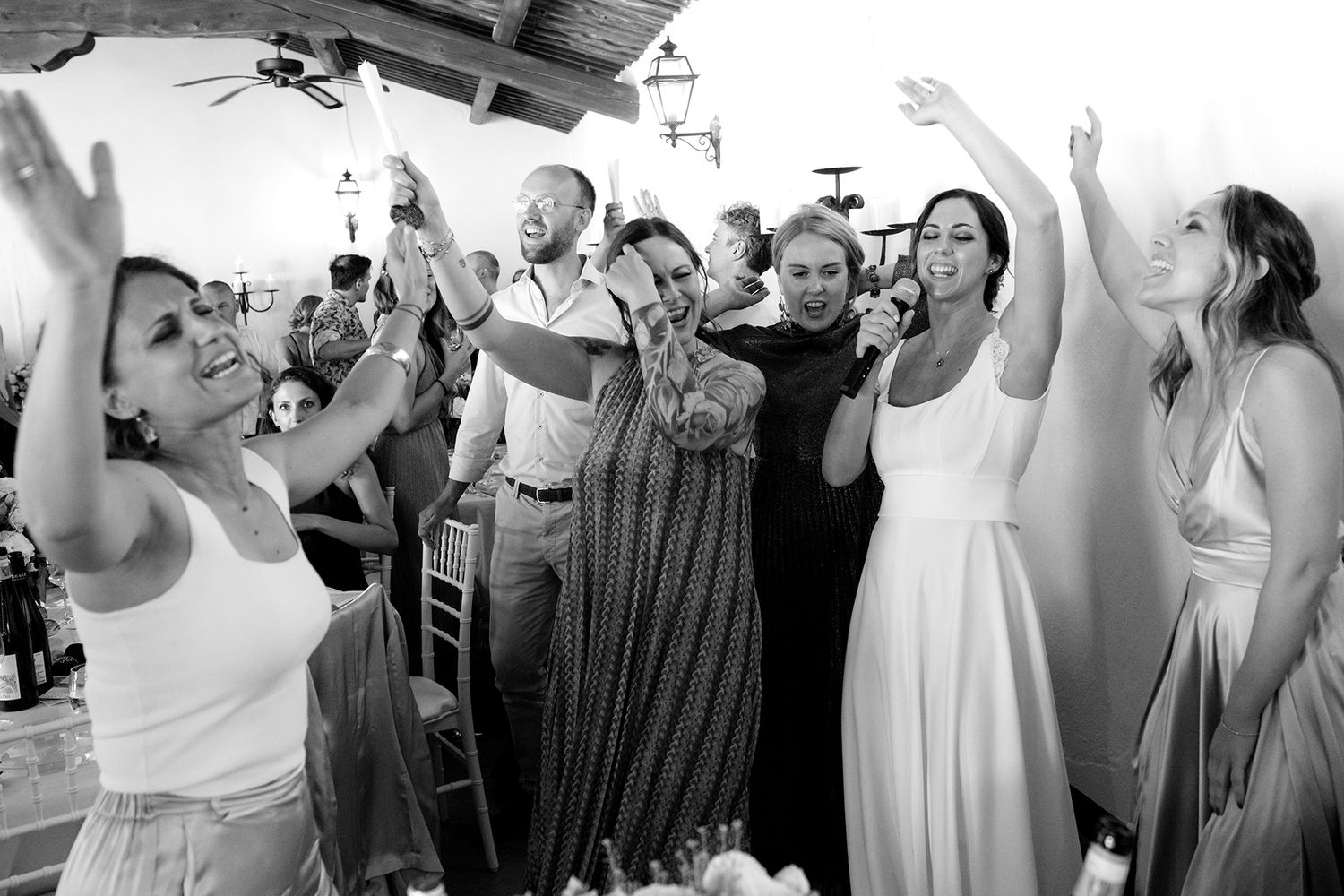Wedding guests in formal attire dancing and celebrating with raised arms at a reception.