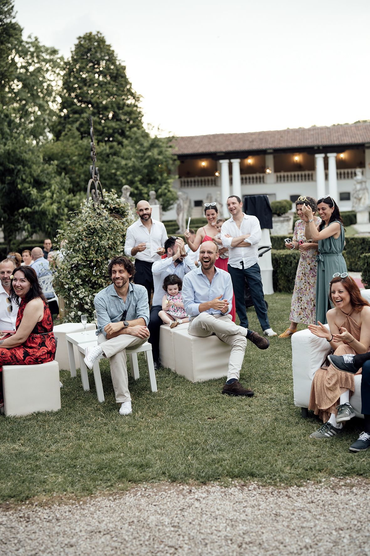 Wedding guests relax on white outdoor seating during an elegant garden reception.