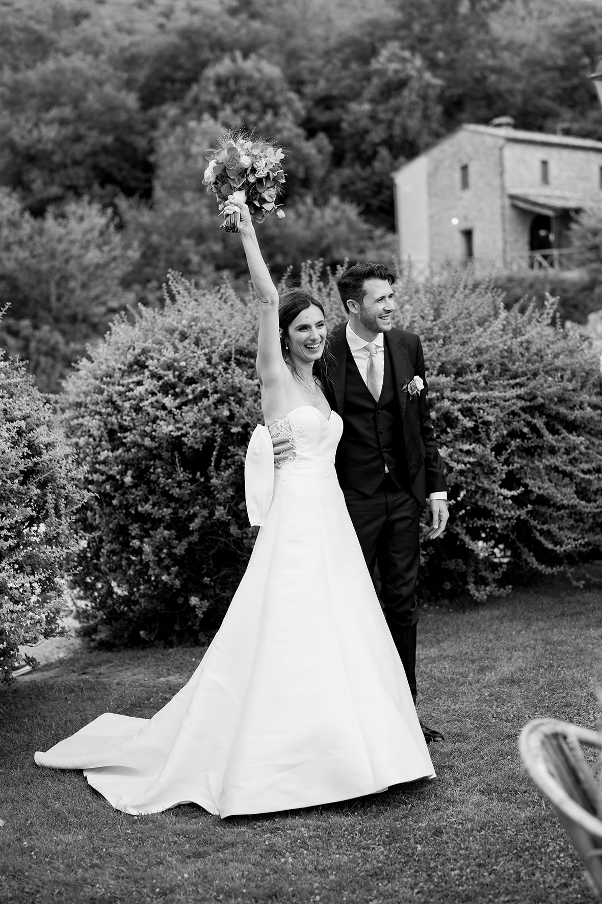 Black and white wedding photos of couple dancing joyfully in a garden setting.