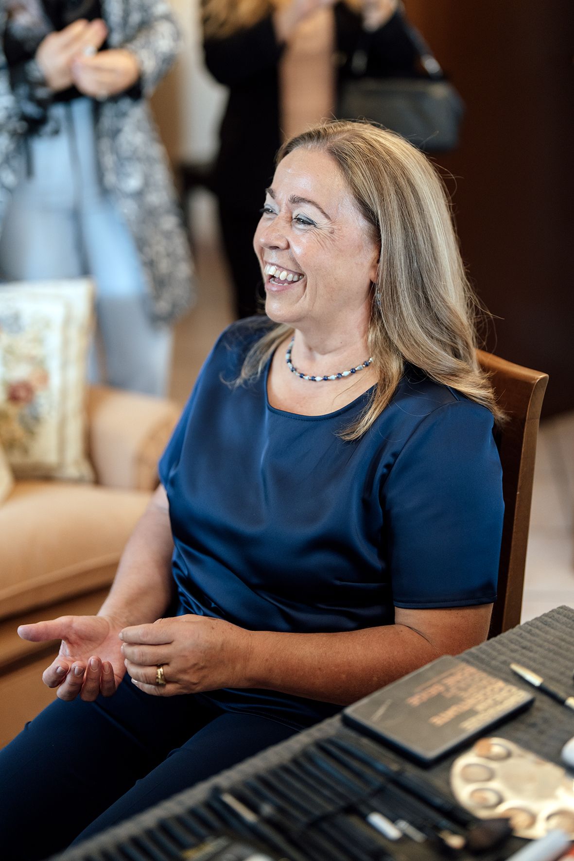 Woman in navy blue top laughing joyfully while seated at a table during a casual gathering.