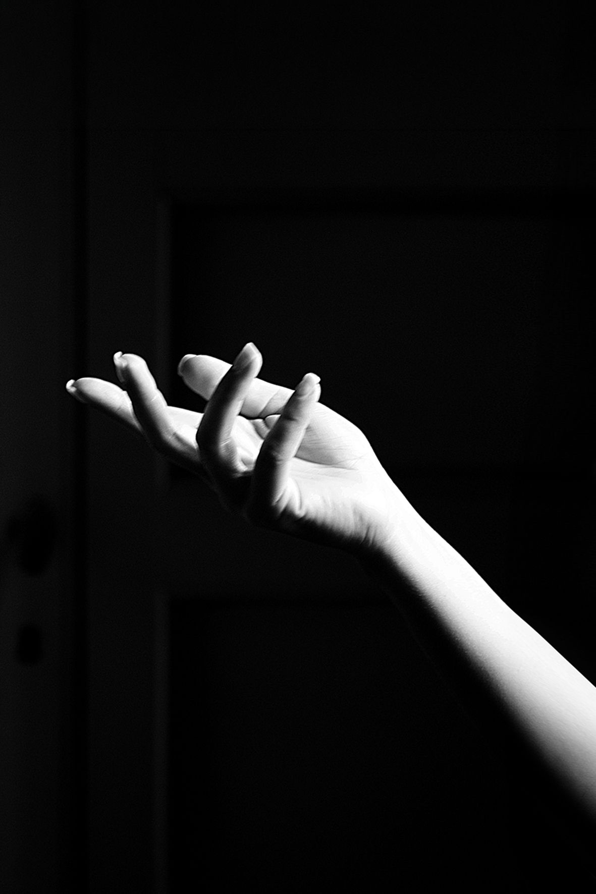 A dramatic black and white photograph of an outstretched hand emerging from darkness with elegant fingers curled.
