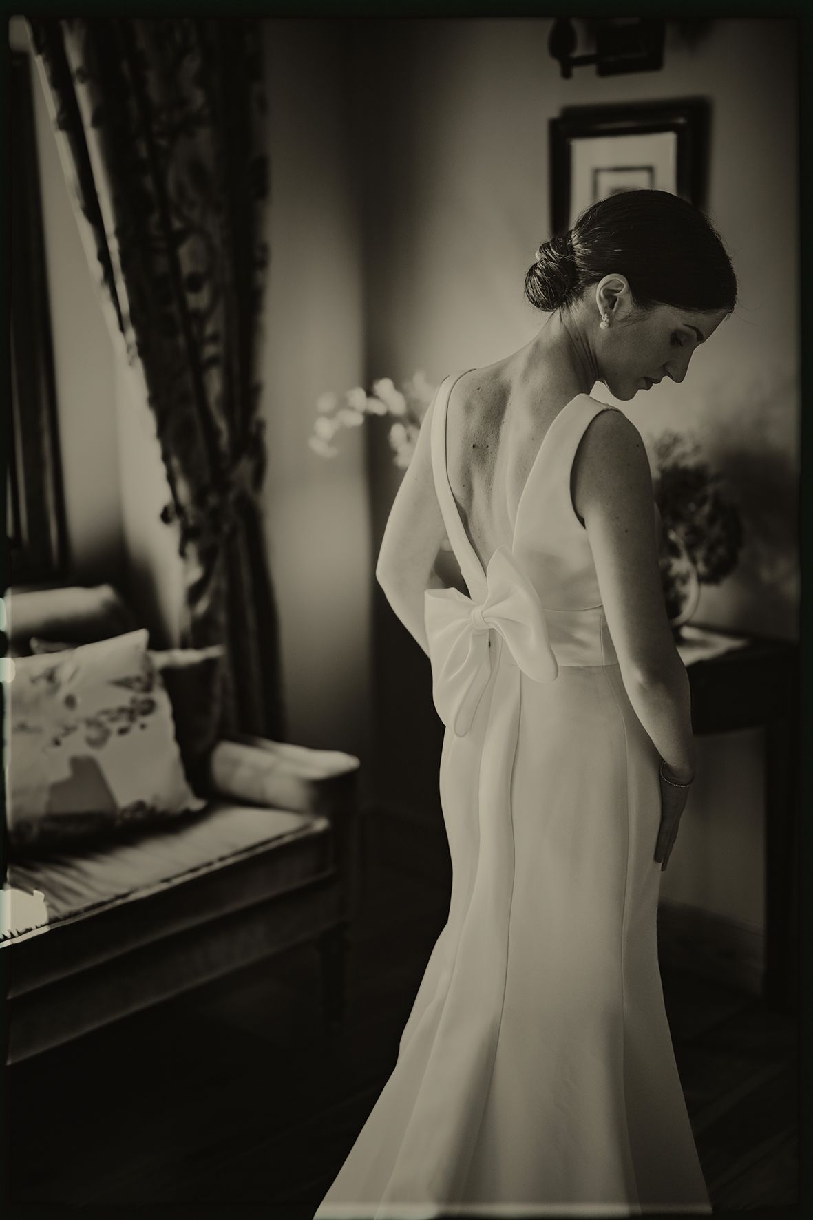 Black and white photo of someone in a white wedding dress getting ready in a dimly lit room.