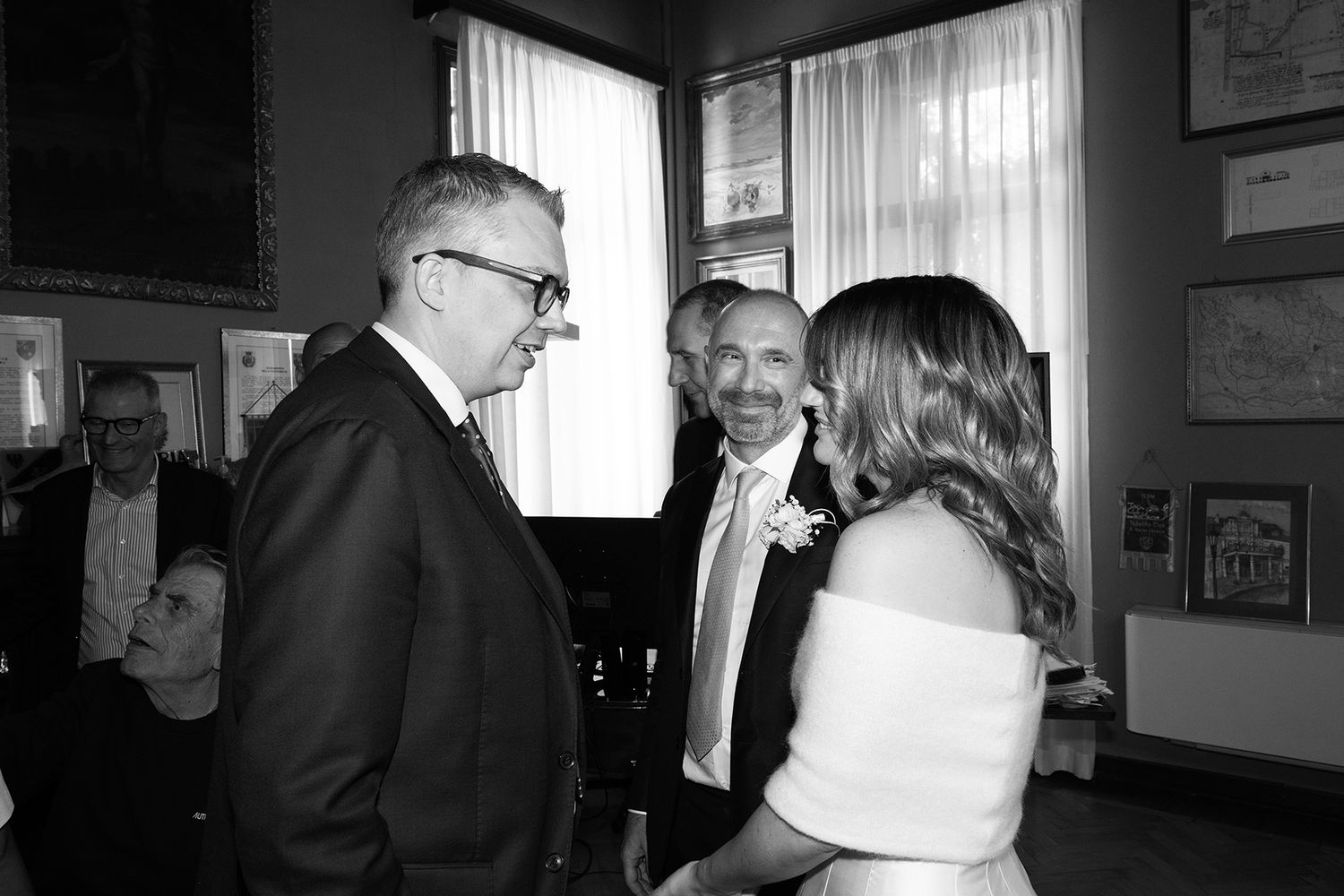 A black and white photo of three people having an animated conversation at a wedding celebration.