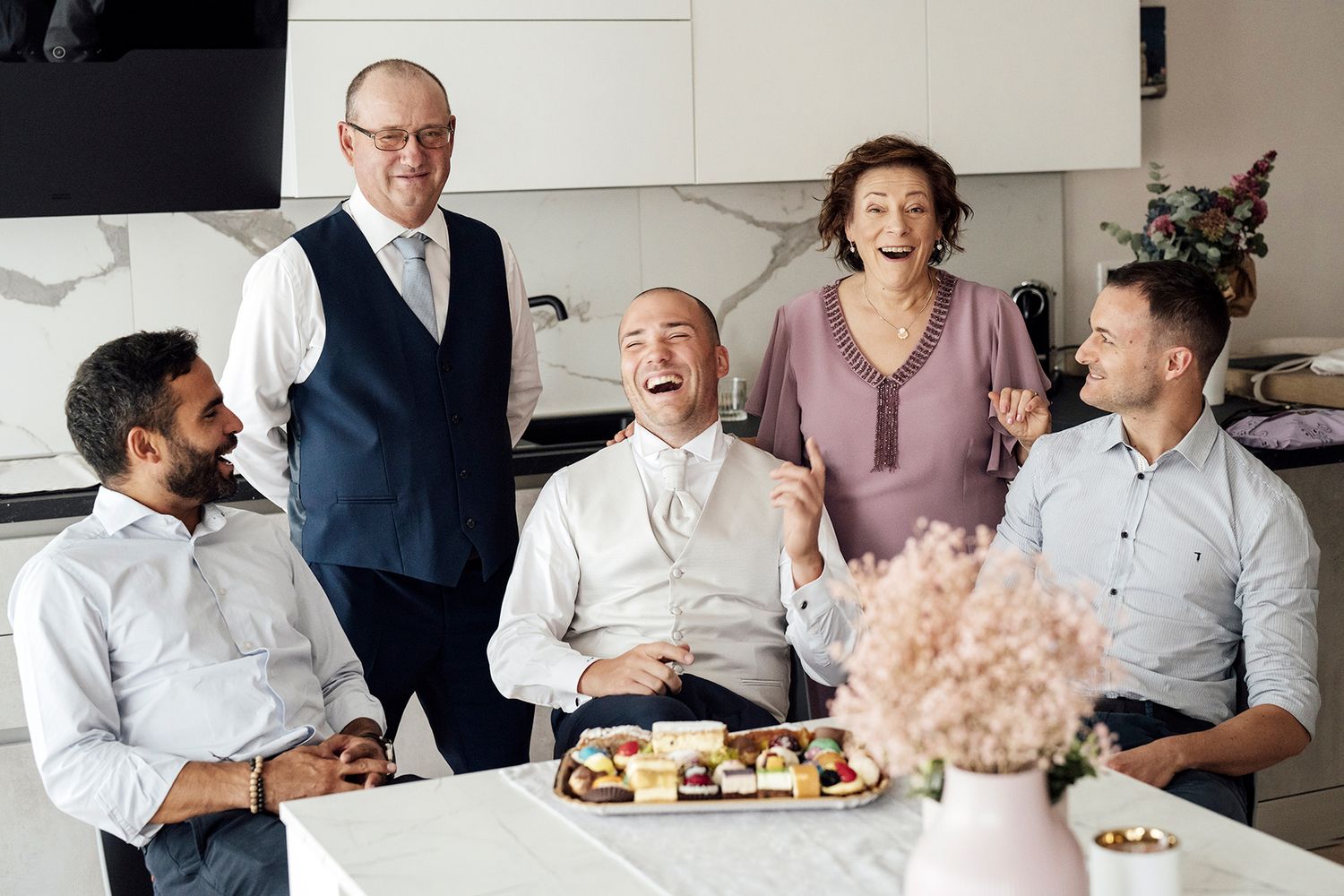 Group enjoys desserts and conversation around kitchen counter during celebration.
