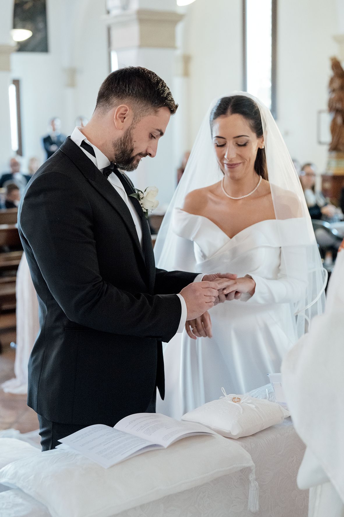A tender moment during a wedding ceremony as the groom places a ring on the bride's finger in an elegant church setting.