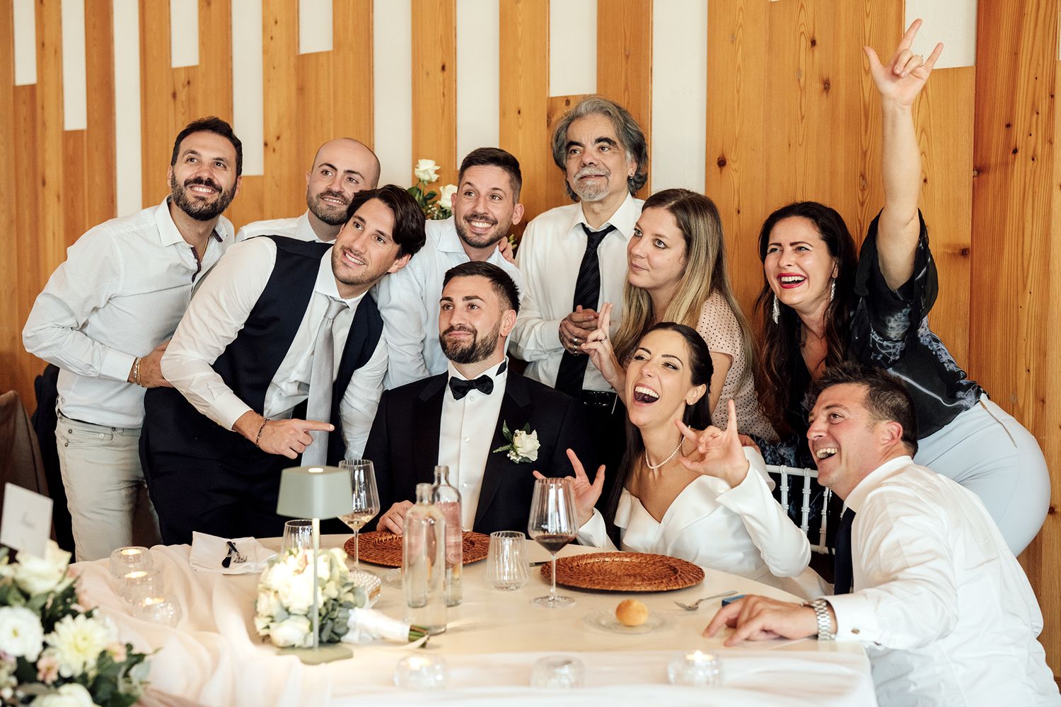 Wedding reception guests seated at long wooden tables celebrating with drinks.