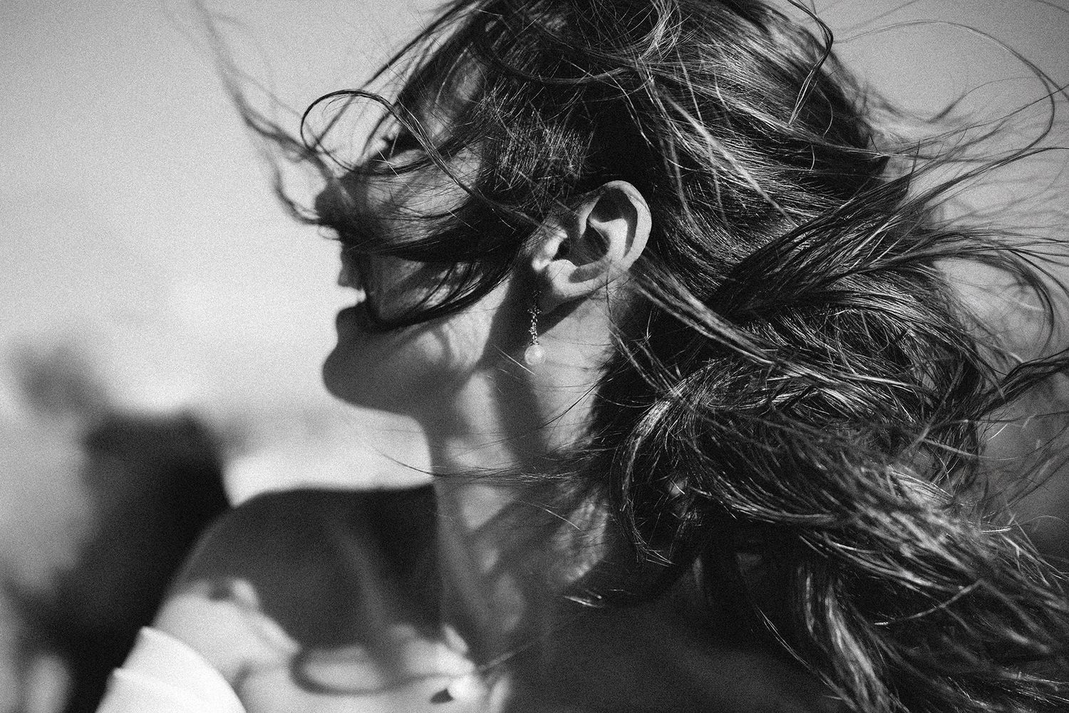 Black and white photo of a woman with windswept hair blowing across her face in dramatic lighting.
