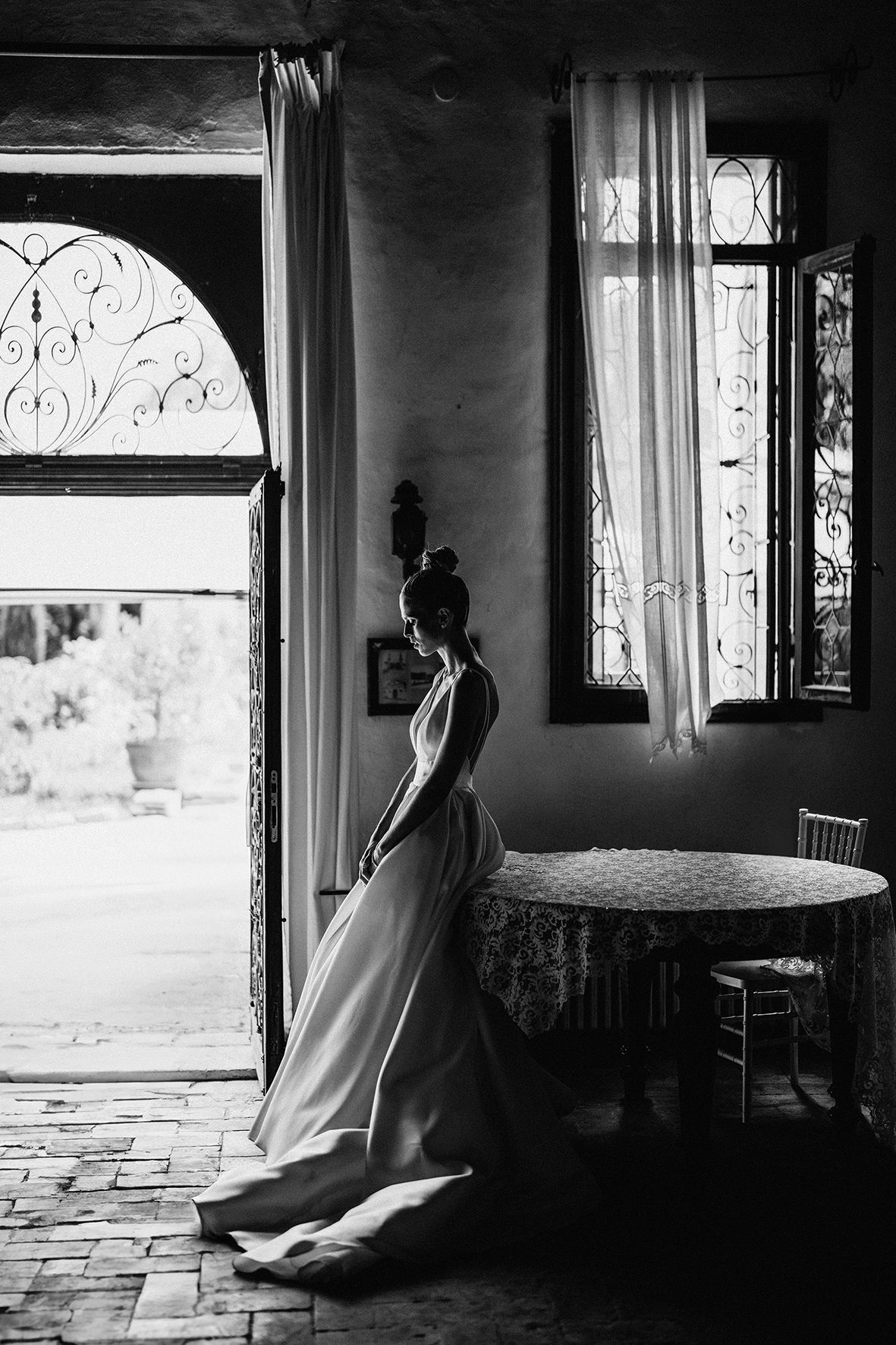 A silhouetted figure in a flowing dress stands in a doorway with an arched window, creating a dramatic black and white scene.