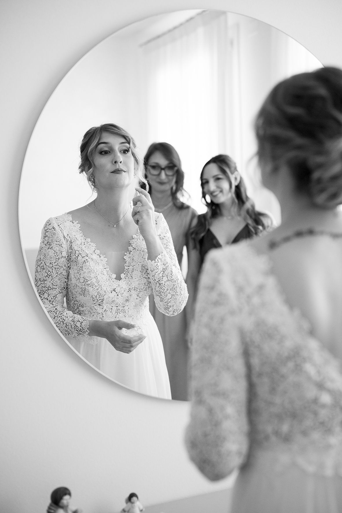 Bride applying makeup in front of circular mirror during wedding preparations.