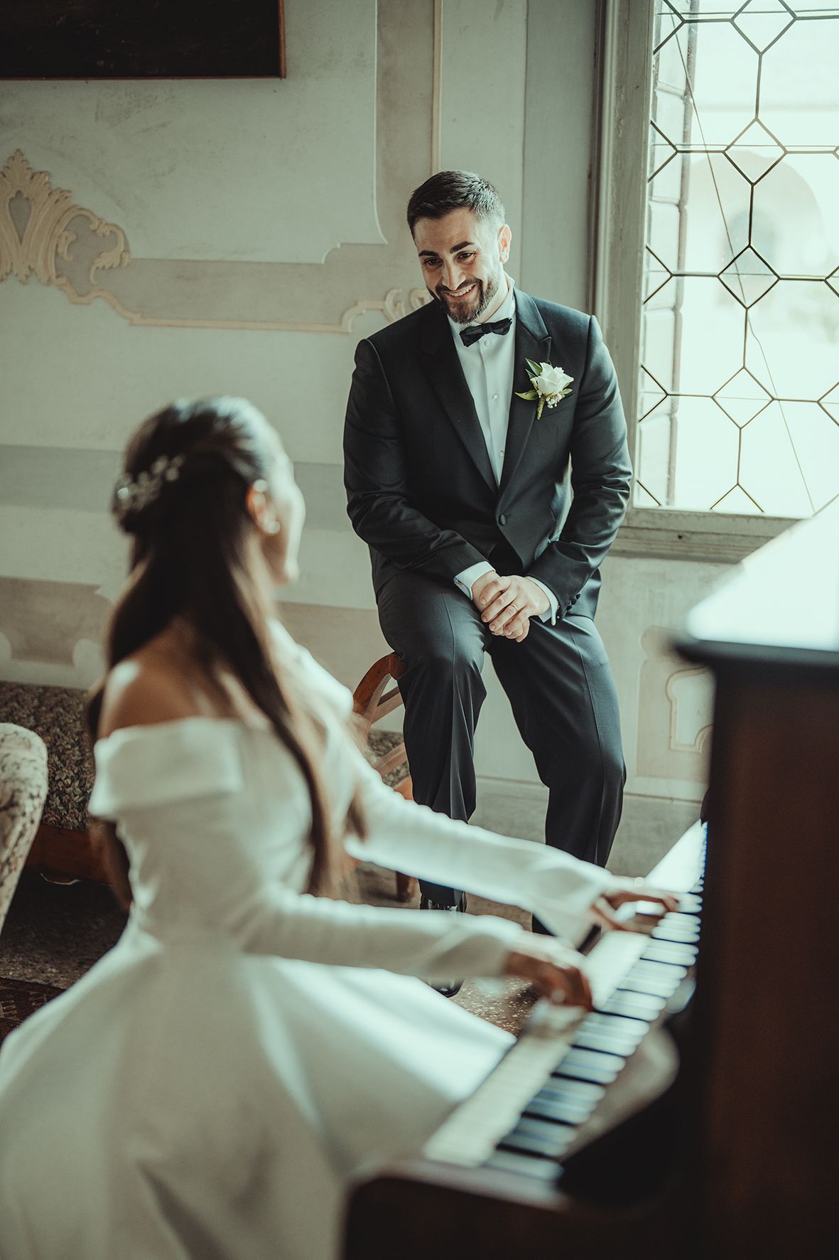 Wedding couple shares playful moments at a piano in an elegant indoor setting.