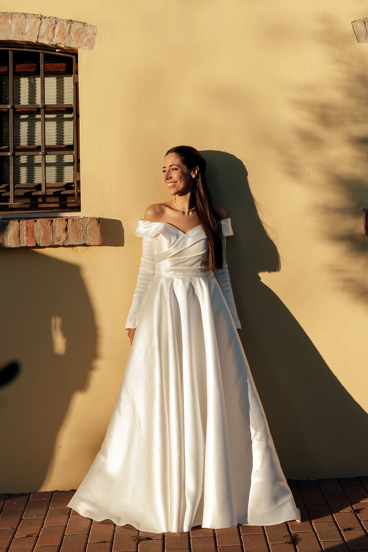 Elegant white wedding dress photographed against yellow wall with dramatic shadows.